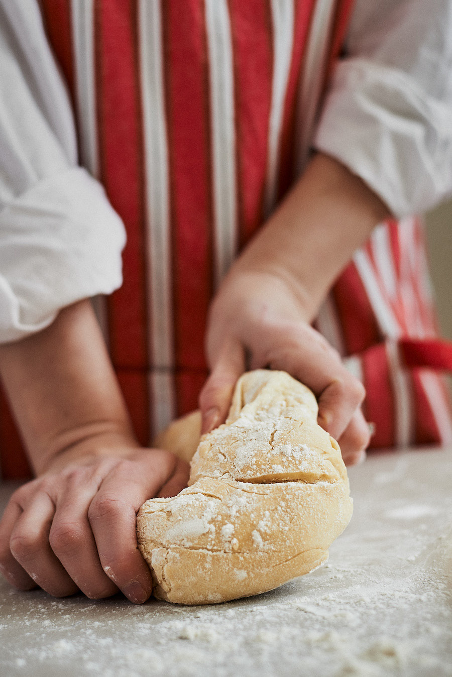 Lifestyle food photography of person kneading a dough in red white striped apron by Montreal photographer Kata Endrodi.