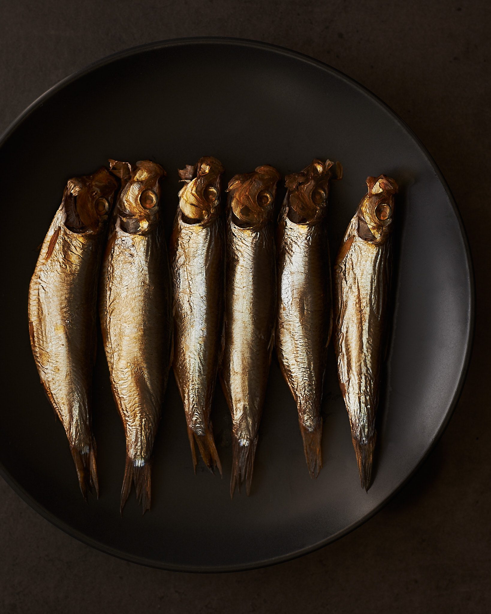 A food photography a bunch of small smoked fish image on black plate , made by Kata Endrodi, a food photographer in Montreal