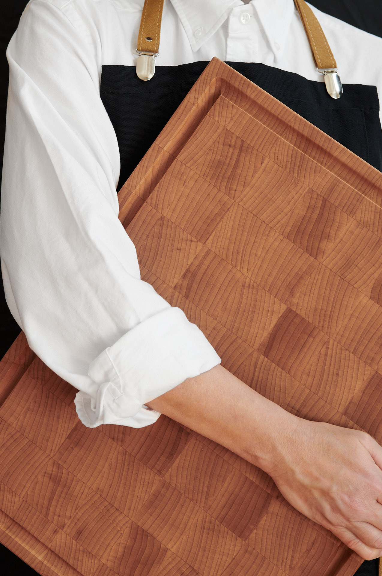 Lifestyle photography featuring a person in an apron holding a maple wooden cutting board, showcasing family culinary moments by Kata Endrodi.