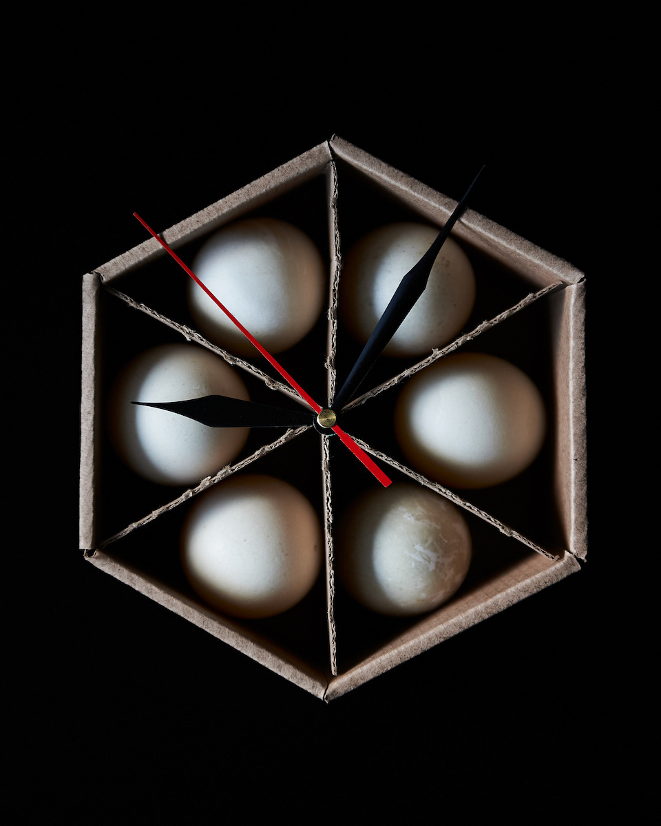 Kata Endrodi Montreal food and product photographer, a food photography siz duck eggs in a hexagonal shape carton with clock dials on black background