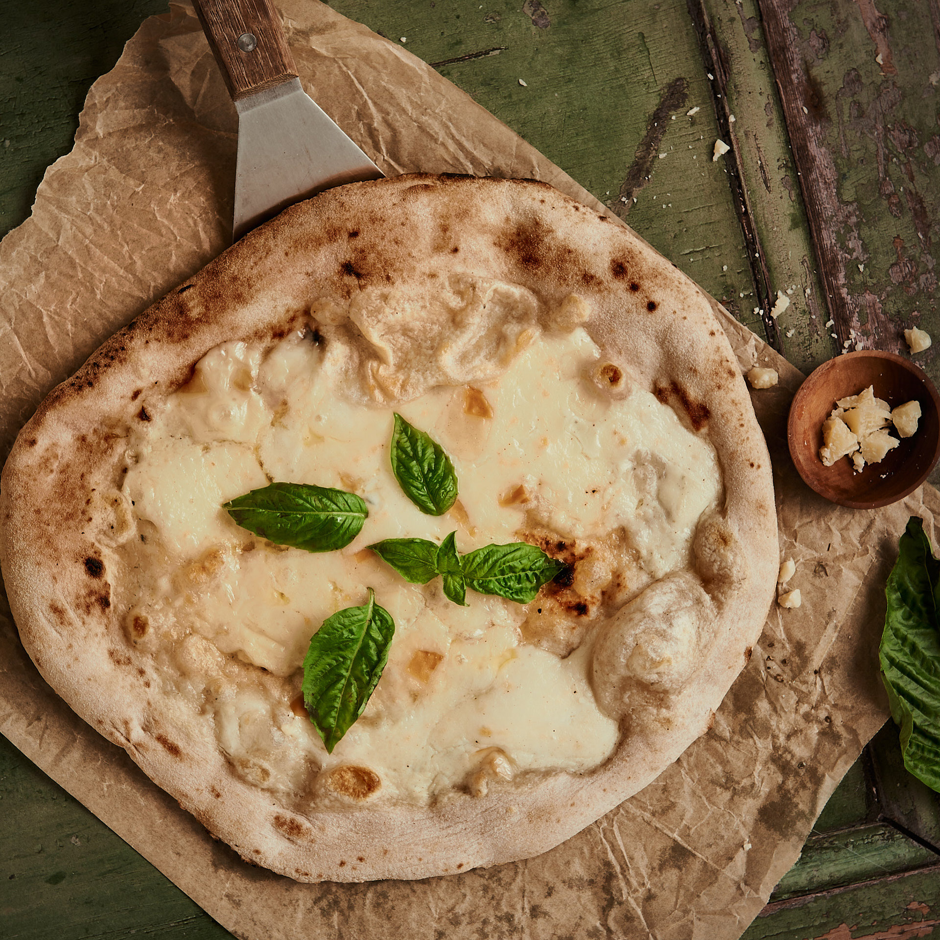 A food product lifestyle photography cheese pizza with basil on green wooden backdrop, made by Kata Endrodi, a food and product photographer in Montreal