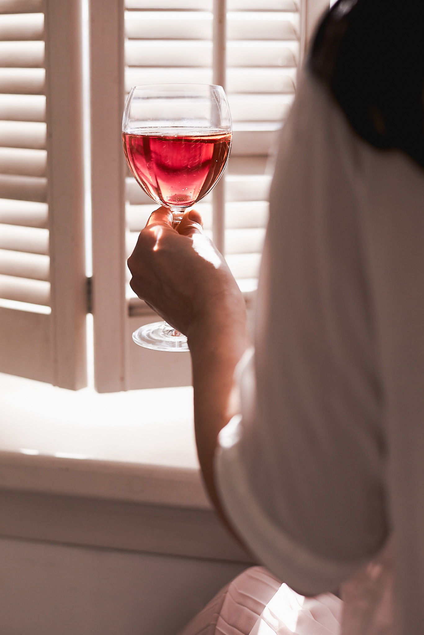 A food photography woman holds a glass with red drink image in front of a window with white shutter, made by Kata Endrodi, a food photographer in Montreal