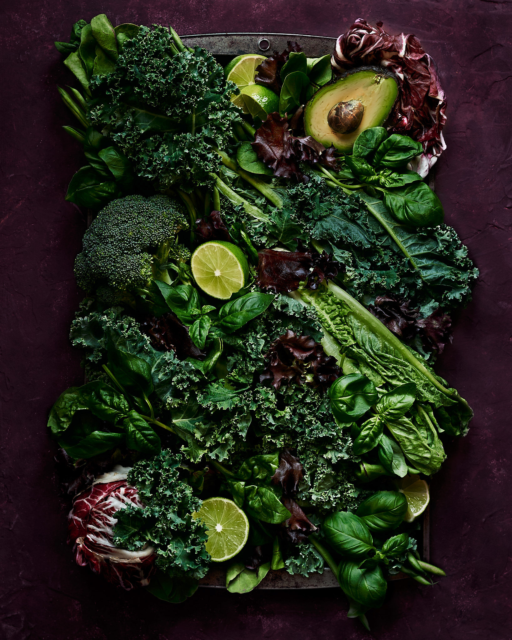 A food photography green fresh produce arrangement in green and dark red on a metal tray and dark red backdrop, made by Kata Endrodi, a food photographer in Montreal