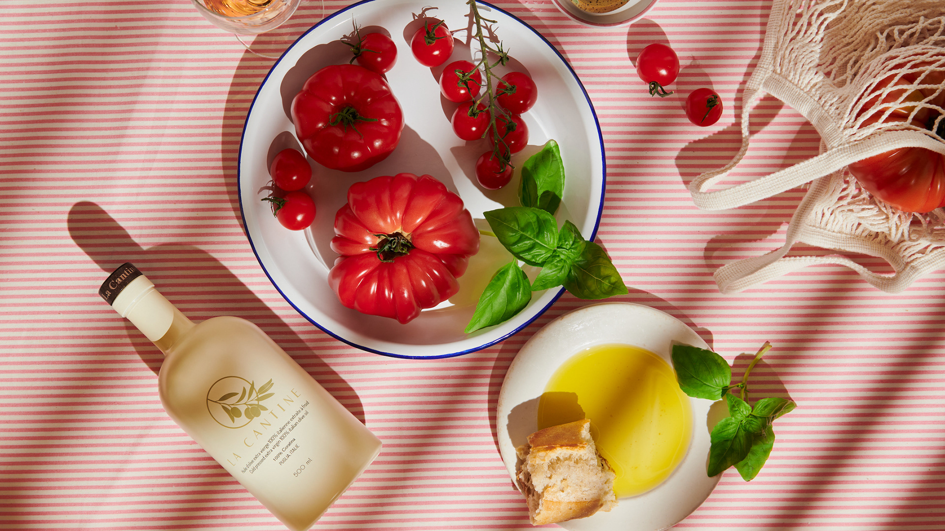 Kata Endrodi Montreal food and product photographer artisanal kitchen lifestyle photography featuring olive oil bottle, plate, tomatoes and shopping bag on a pink and white background