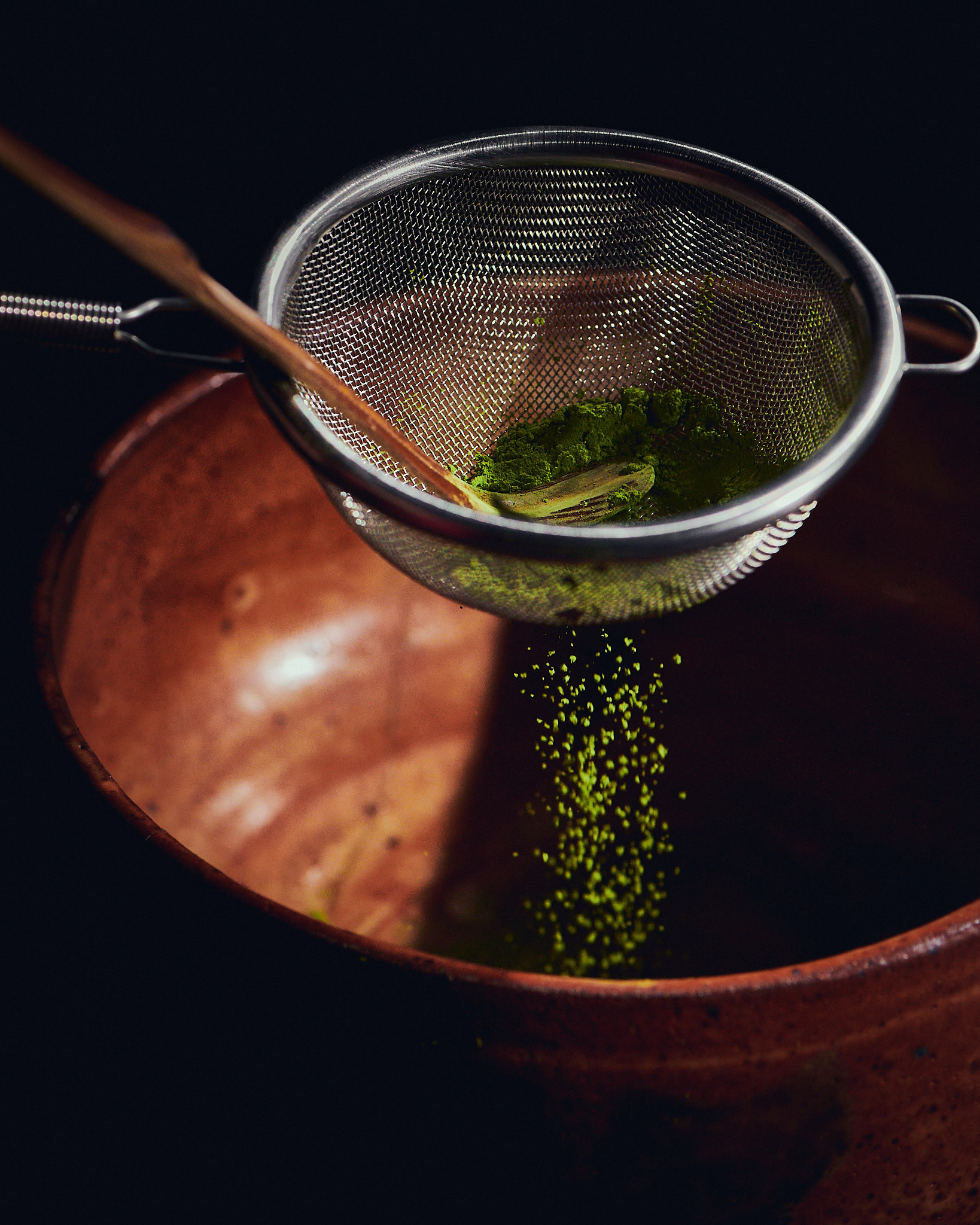 Kata Endrodi Montreal food and product photographer, lifestyle photography featuring a sifter above a brown handmade ceramic bowl with green matcha powder and a wooden matcha stick