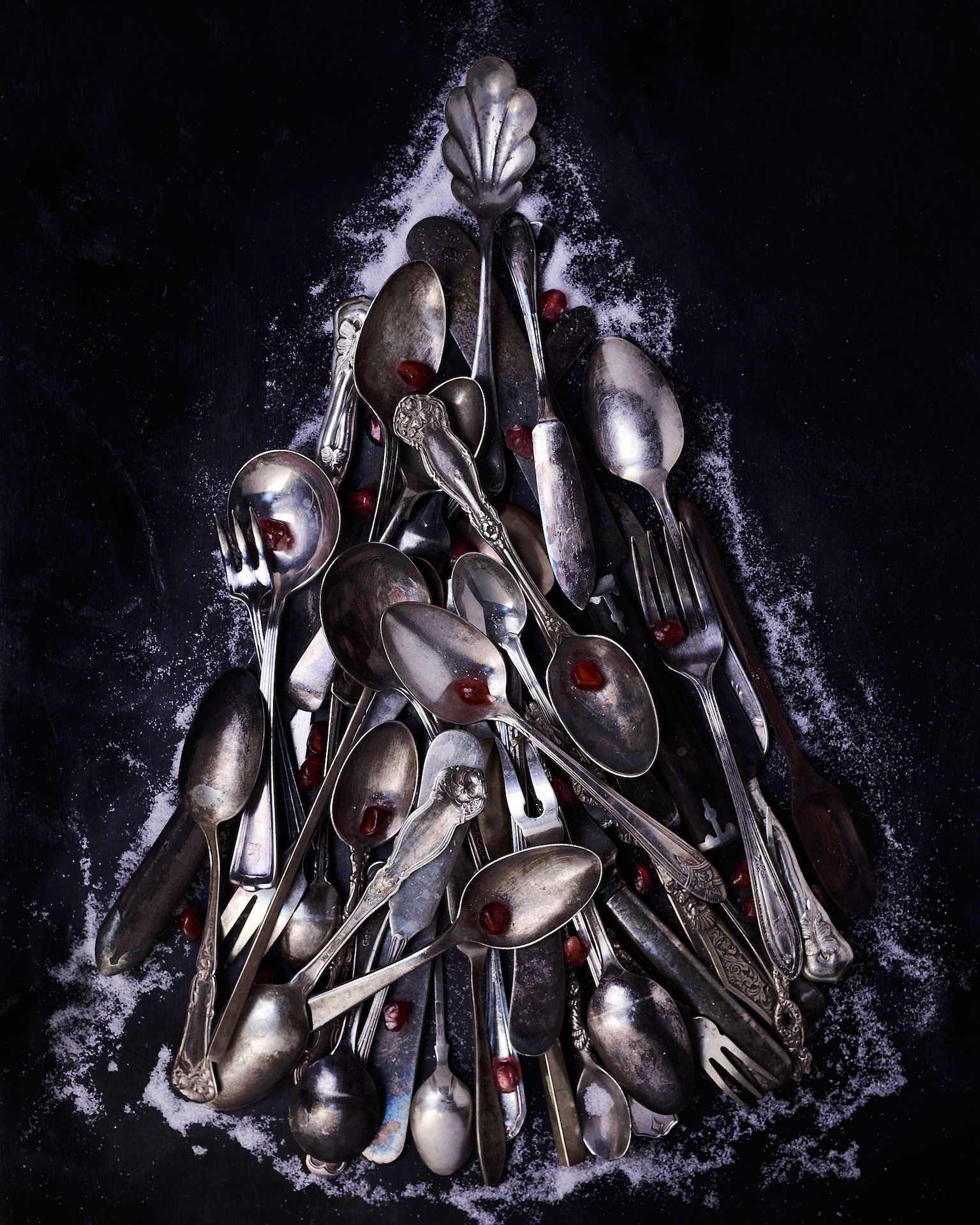 A food photography  vintage silverware image in a Christmas tree shape, with some pomegranate arils and white granulated sugar around it on black backdrop, made by Kata Endrodi, a food photographer in Montreal 