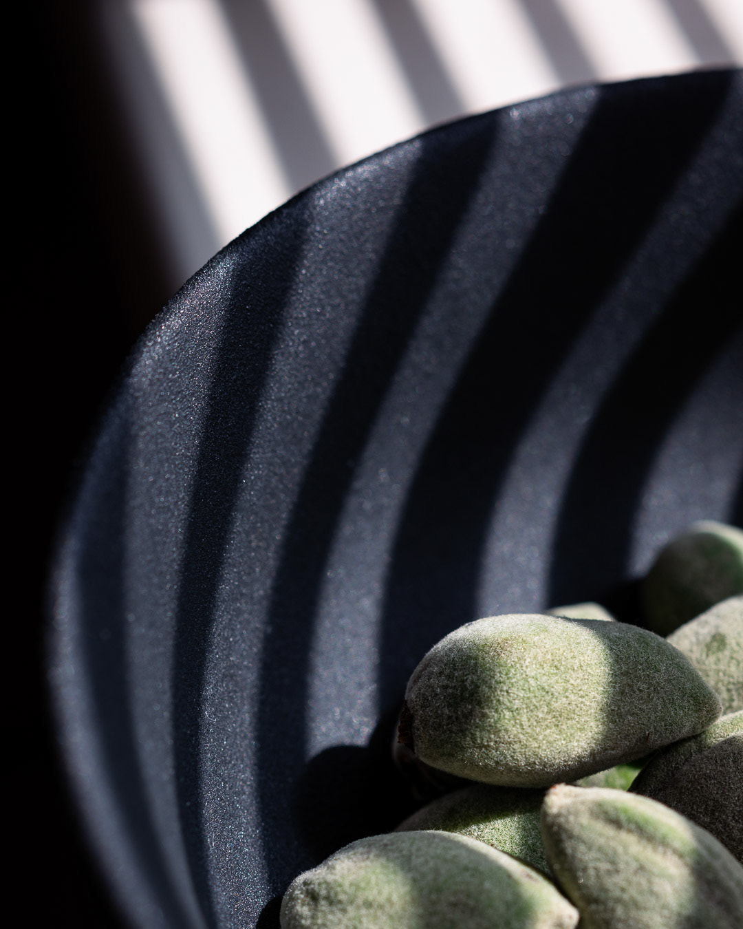 A food photography green almonds image in black bowl in hard light, made by Kata Endrodi, a food photographer in Montreal