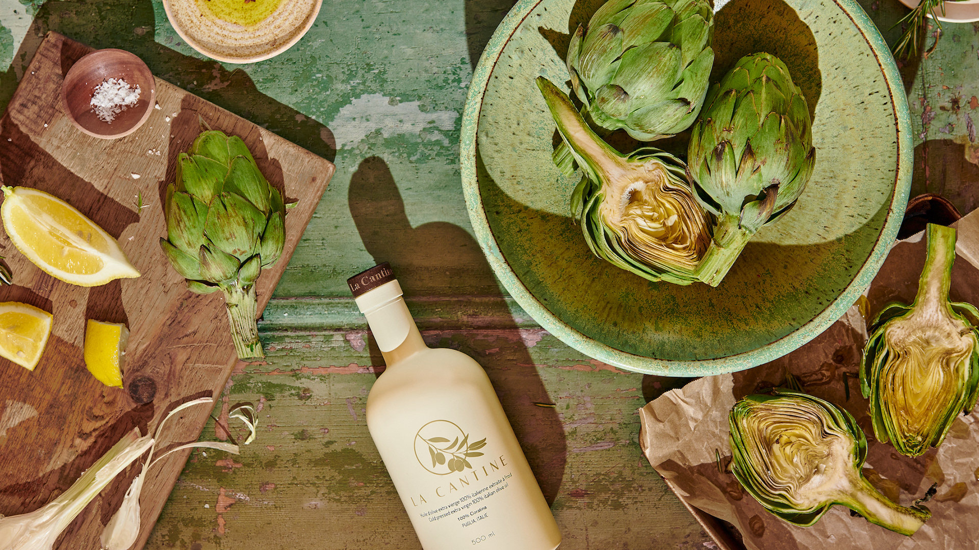  Kata Endrodi Montreal food and product photographer artisanal kitchen lifestyle photography featuring olive oil bottle, green bowl and cutting board with artichokes and lemon on weathered green backdrop