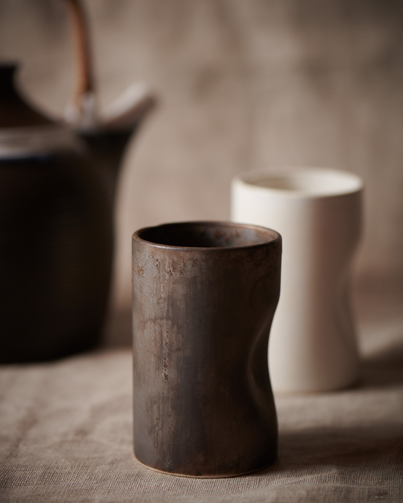 Kata Endrodi Montreal food and product photographer, lifestyle photography featuring a brown and a white handmade Japanese mug and a brown teapot with bamboo handle at the back on a neutral linen surface. 