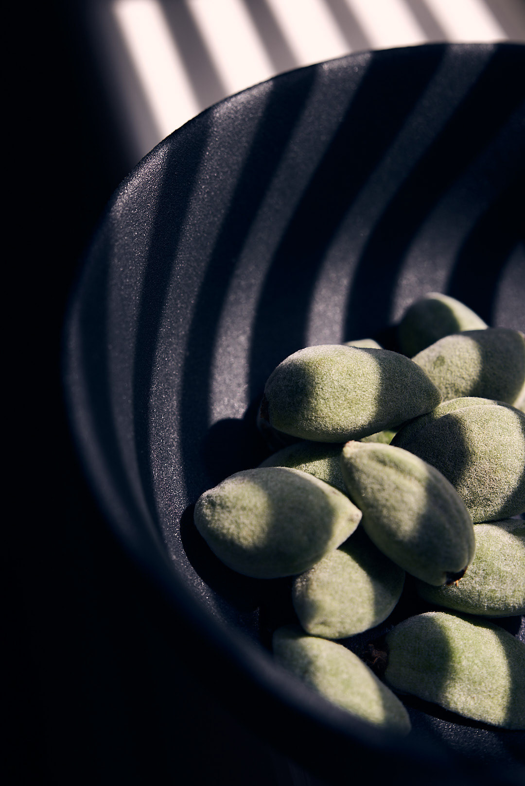 A food photography of green almonds in a black bowl, made by Kata Endrodi, a food photographer in Montreal