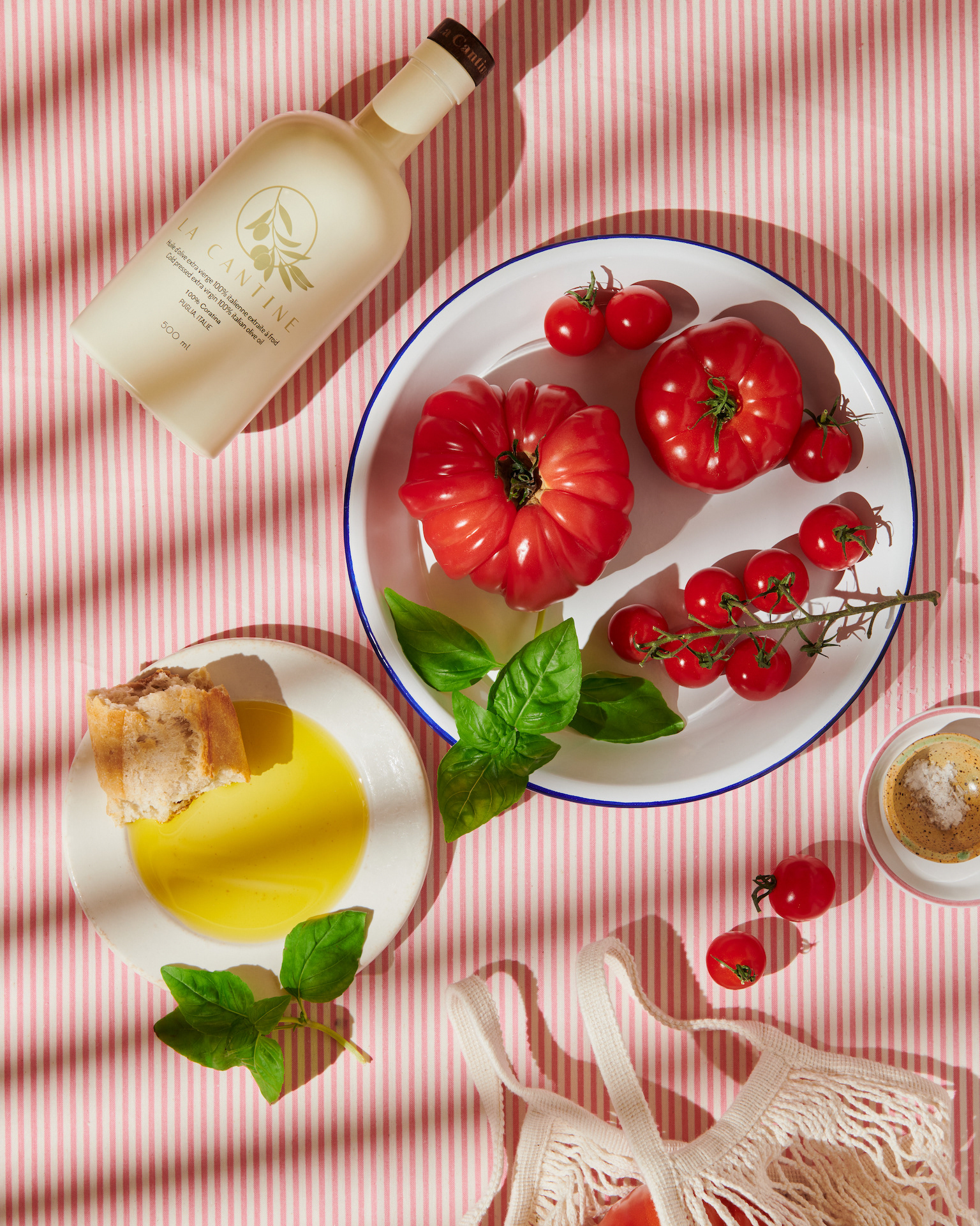 Kata Endrodi Montreal food and product photographer artisanal kitchen lifestyle photography featuring olive oil bottle, plate, tomatoes and shopping bag on a pink and white background