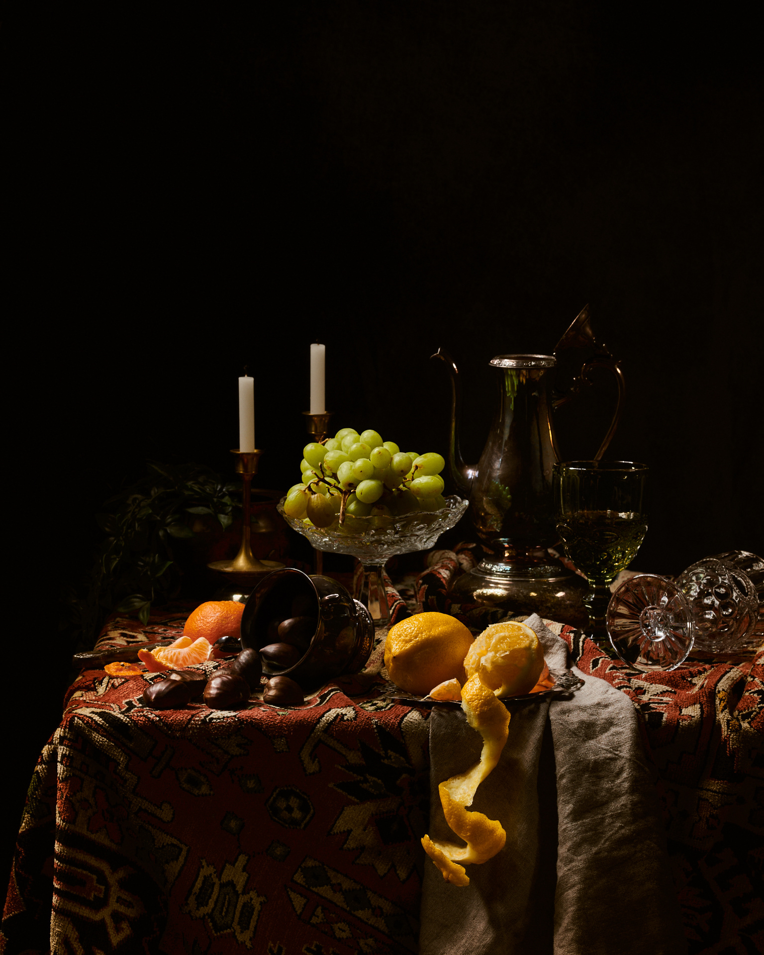 Kata Endrodi Montreal food and product photographer, Dutch Master-inspired still life featuring green grapes, citrus, and chestnuts on a patterned tapestry, with dramatic chiaroscuro lighting and vintage silverware.
