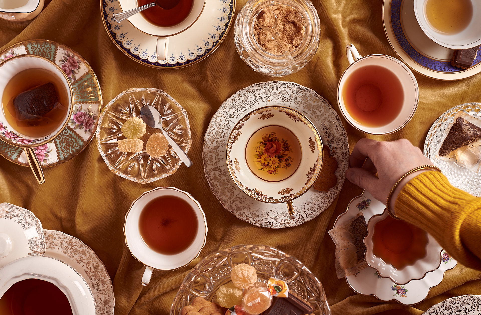 A food photography table set tea party image with vintage cups, saucers on dark yellow velvet background, made by Kata Endrodi, a food photographer in Montreal