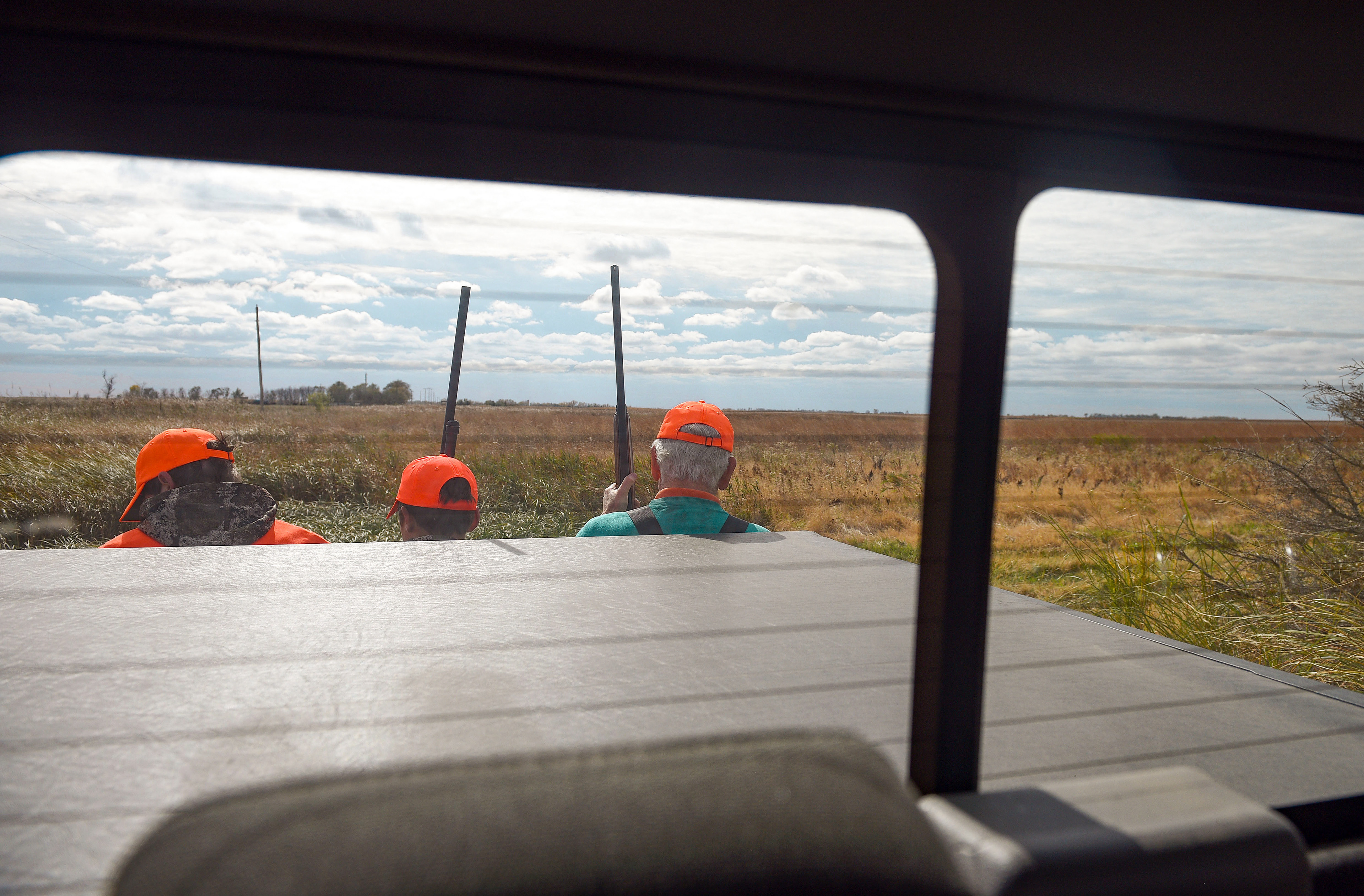 Noah Watson, Gavin Johnson and Don Bierle hitch a ride on the back of a pickup truck during the pheasant season opener on Saturday, October 17, 2020, near Olivet, South Dakota.