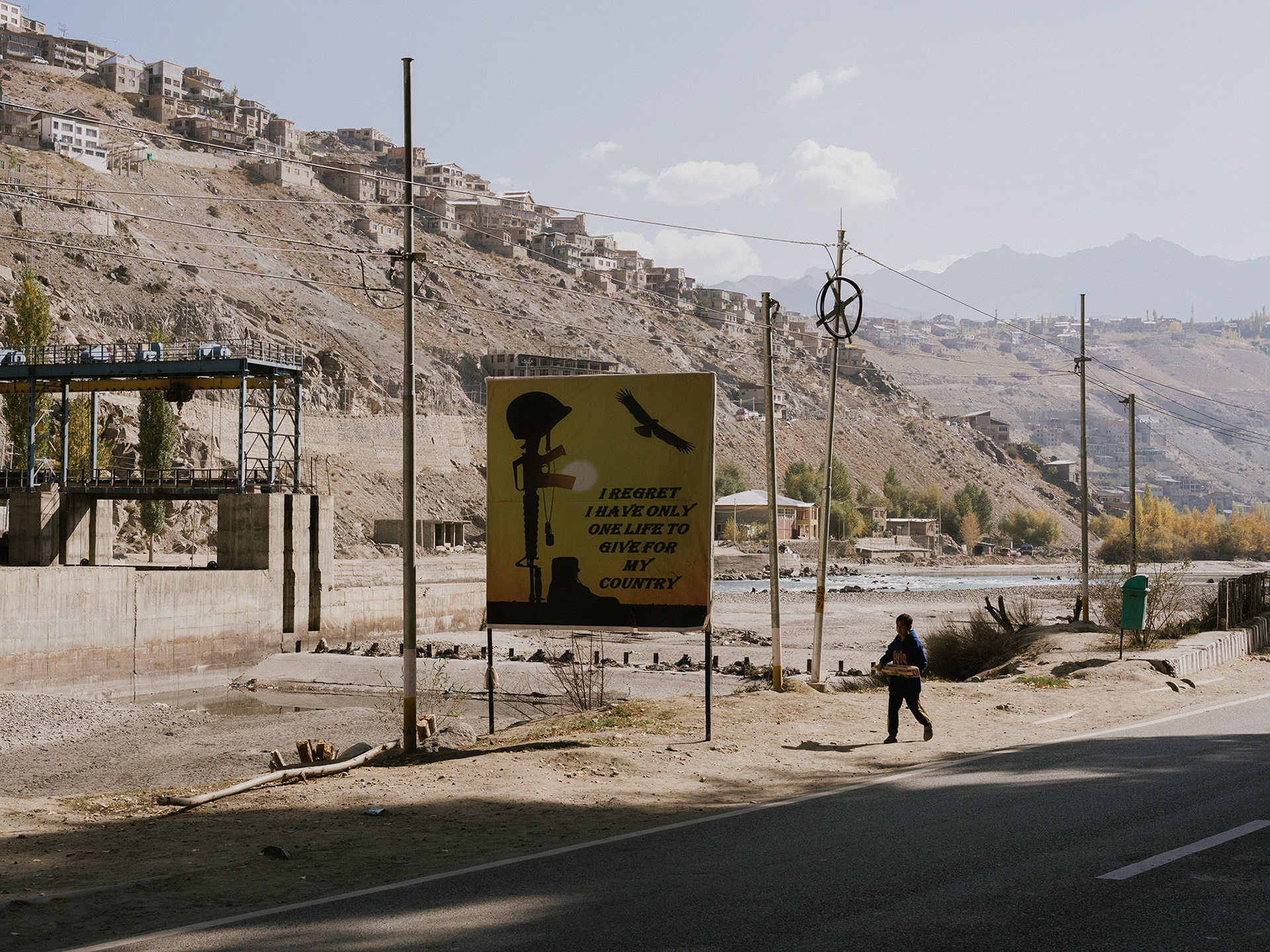 A kid walking along the river in Kargil with a cricket bat. Being right on the Line of Control, the city has been subject to border clashes and wars since the partition.