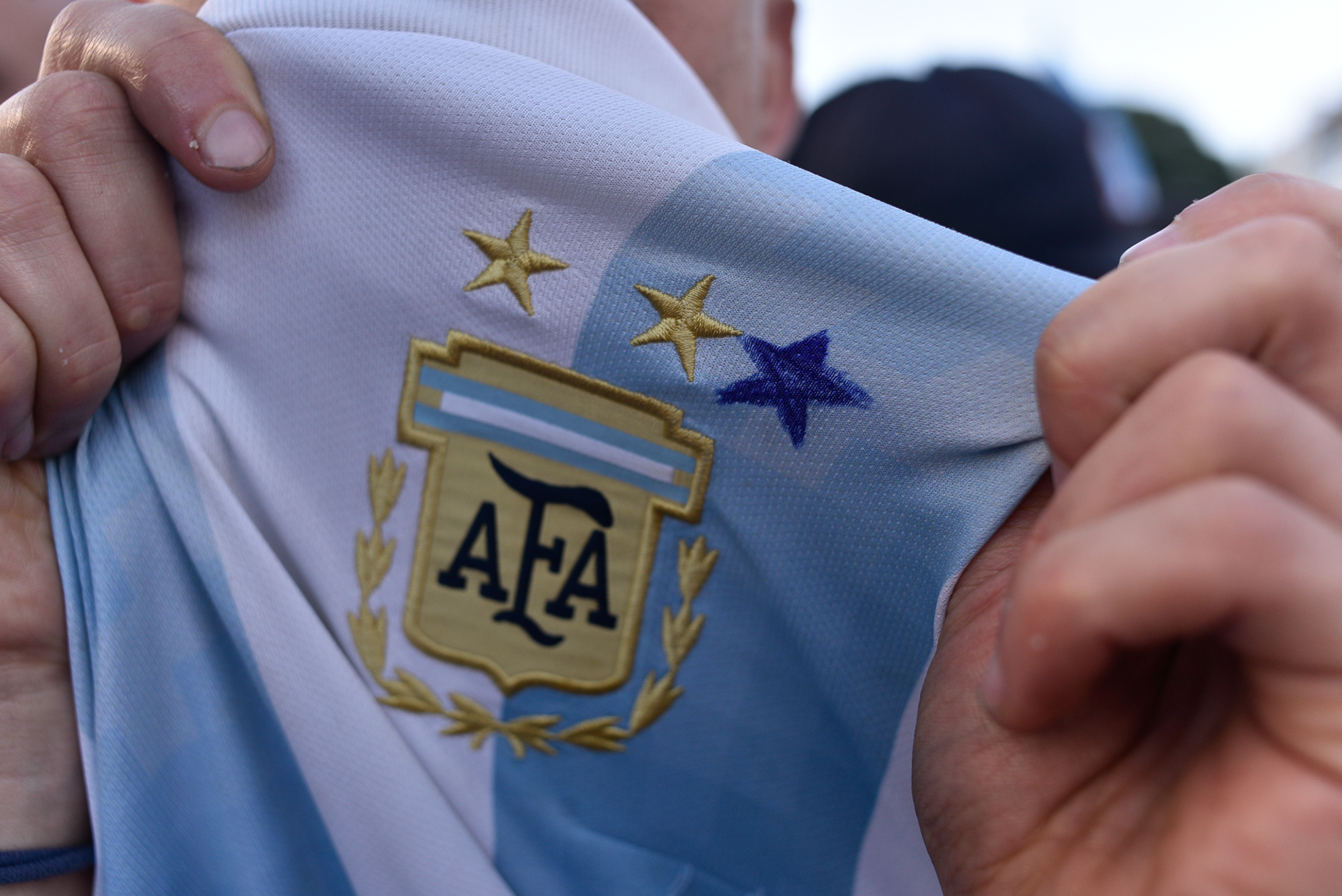 Poseído por la urgencia de la historia, un hincha interviene el escudo de la Albiceleste, dejando un rastro indeleble con la tinta que proclama, "Soy el testigo de la Inmortalidad"
