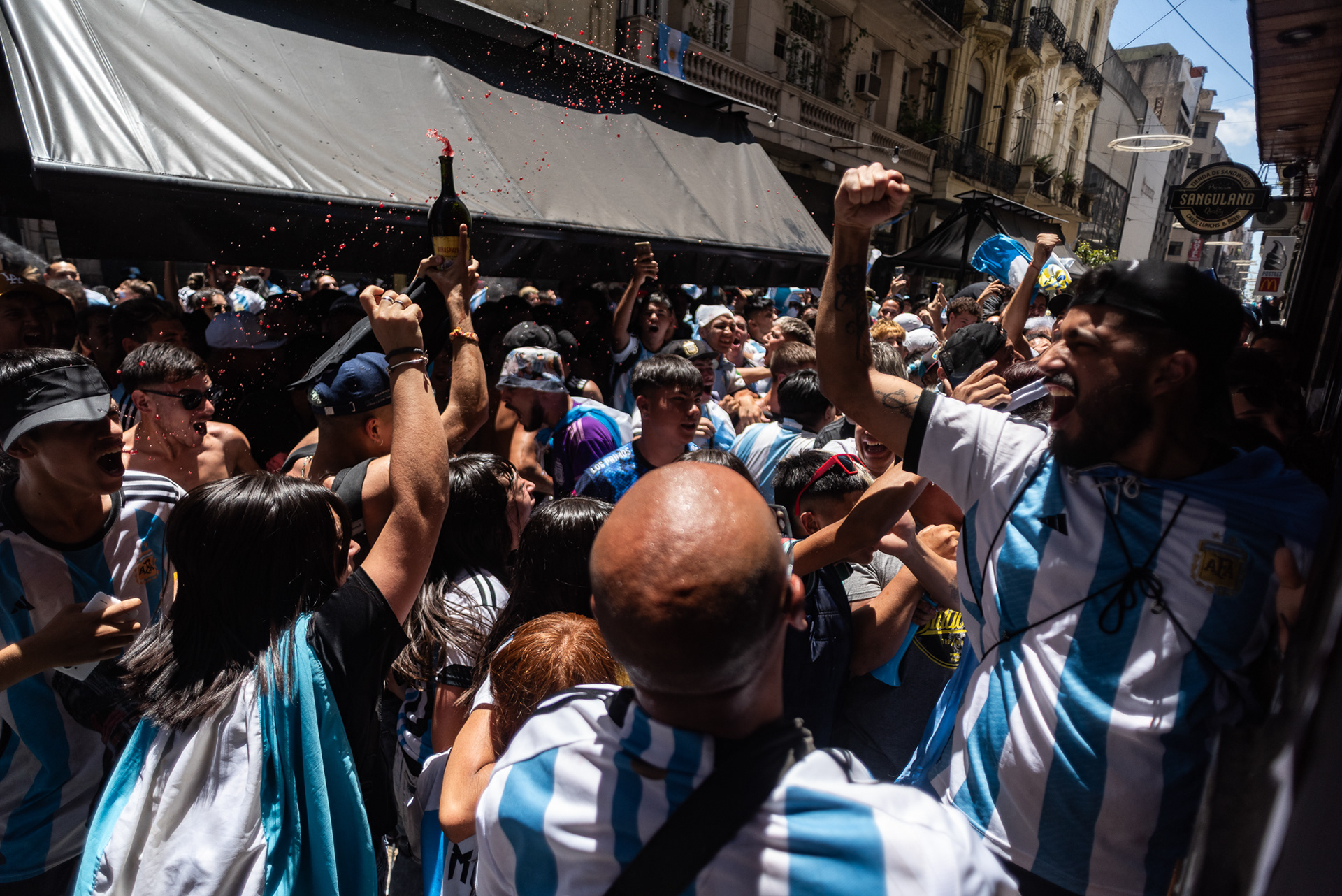 Apenas la red se infla con el penal de Montiel, un grito visceral se ahoga mientras el vino vuela libre, rociando a la multitud como un bautismo de gloria.