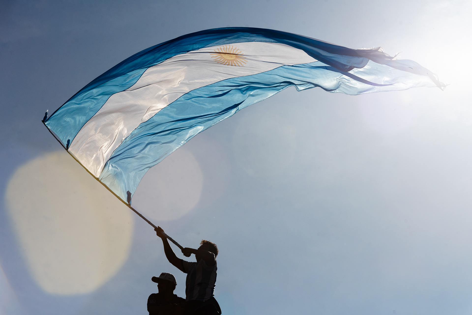 En la hora dorada de la conquista, un hincha es ungido por el sol, y al flamear la bandera, la convierte en un símbolo vibrante, el último destello del día que se hizo eterno.