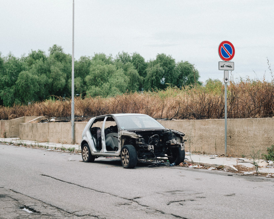 A wrecked and burned car, abandoned on the street.