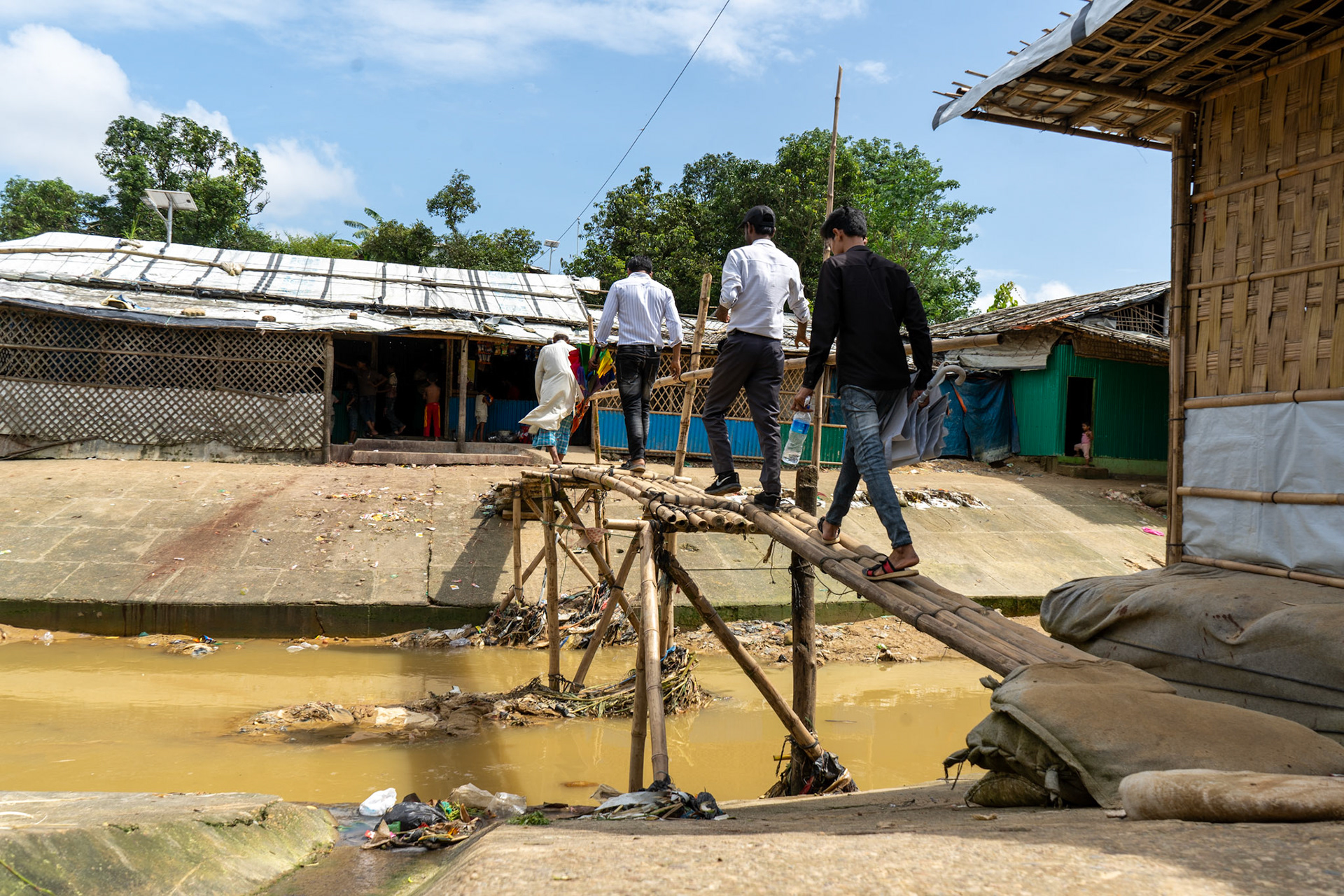Four Rohingya refugees cross a bridge over the camps only sewage system