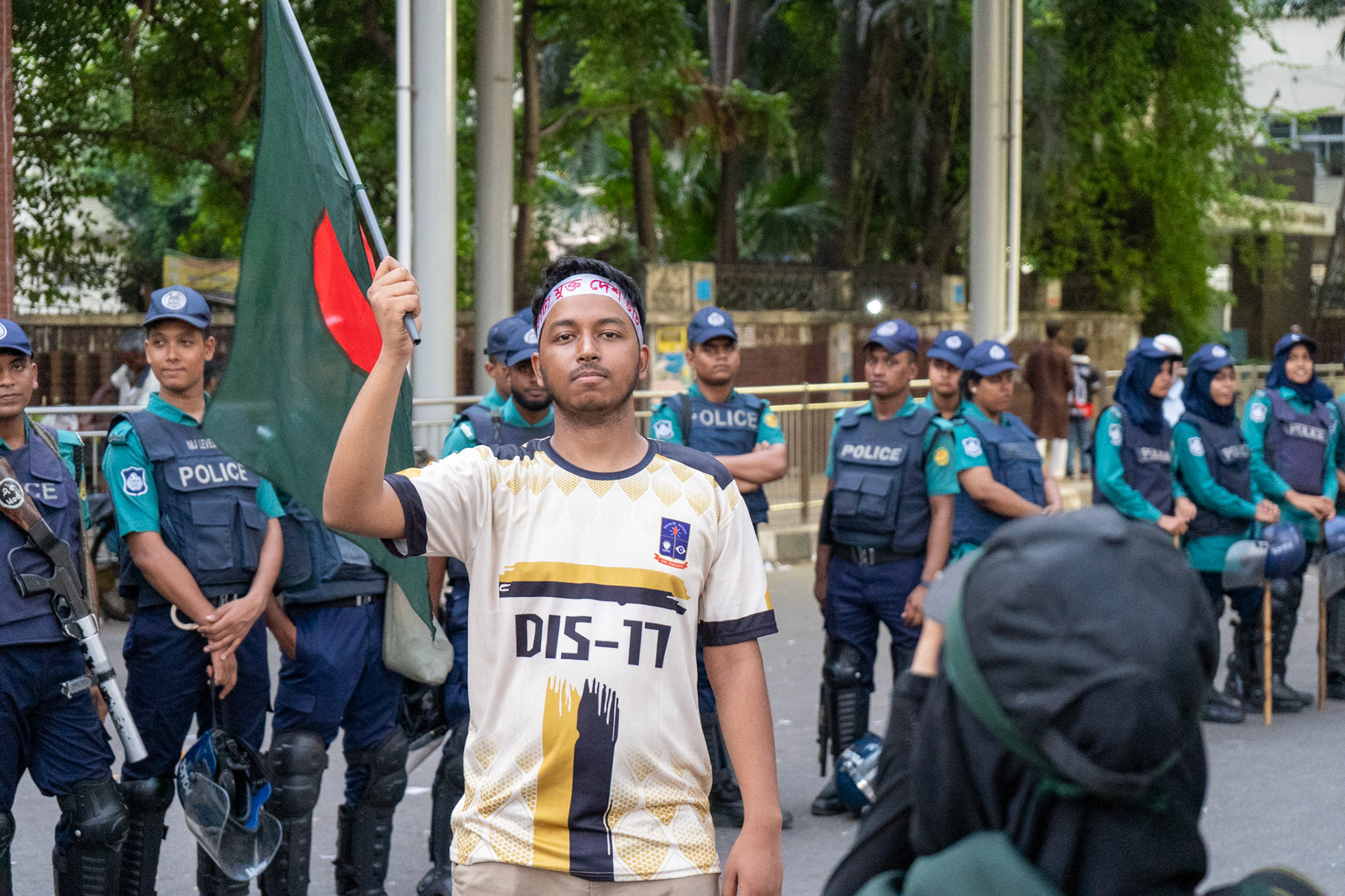 A Dhaka University student waves the Bangladeshi flag in front of the police, just days before police began their massacre of 1,400 students in reaction to the Quota protests in June 2024
