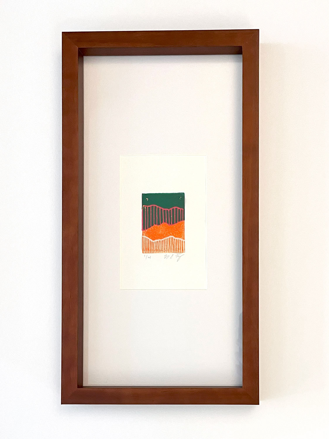 A small abstract linocut print in a long, narrow frame with a white mat. The print is divided into four sections alternation between shaded vertical lines and sections of solid color. 