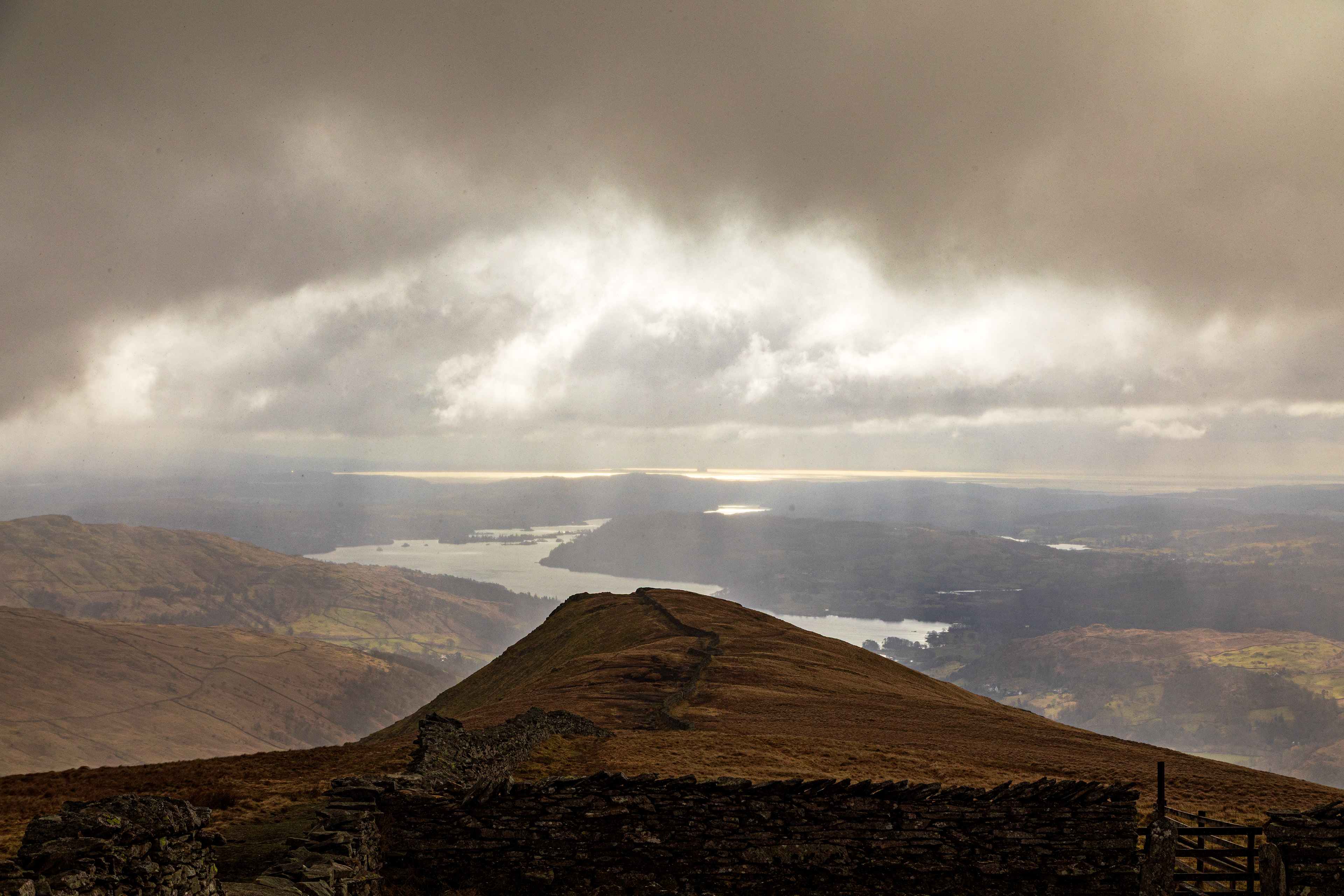A view from the top of a mountain showing sunlight through clouds onto lakes