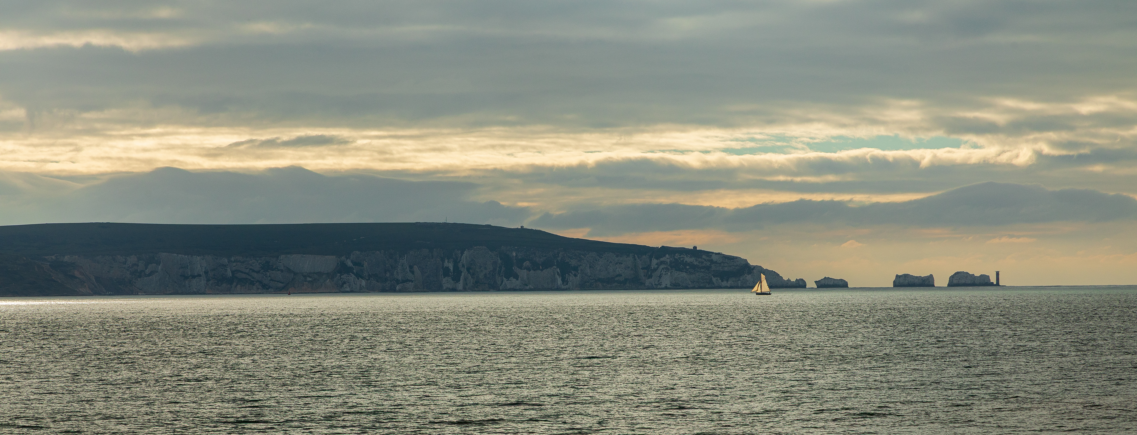 Looking across the Solent to the Isle of Wight with the sails of a yacht picked out by the sun
