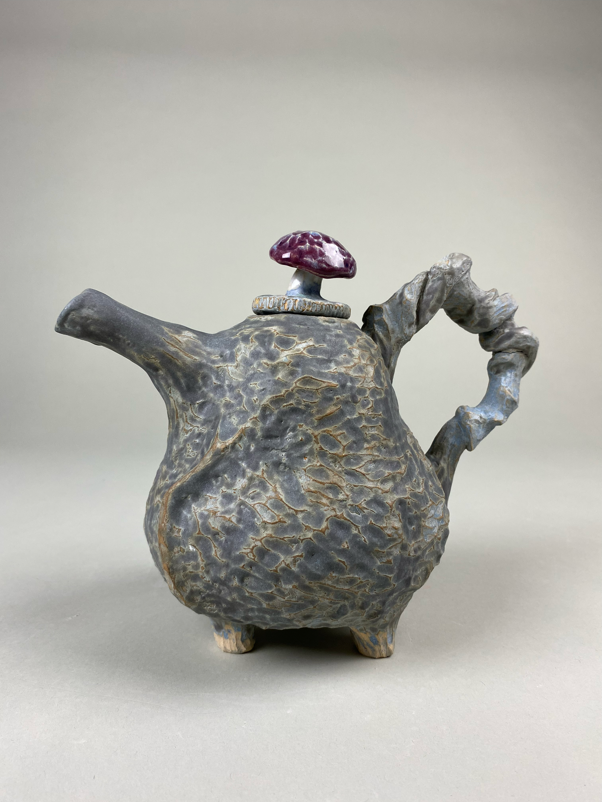 The body of the teapot is colored with underglaze to emphasize the grooves of the wood-like texture. But the handle, a simple mushroom motif, has a glossy raspberry glaze.