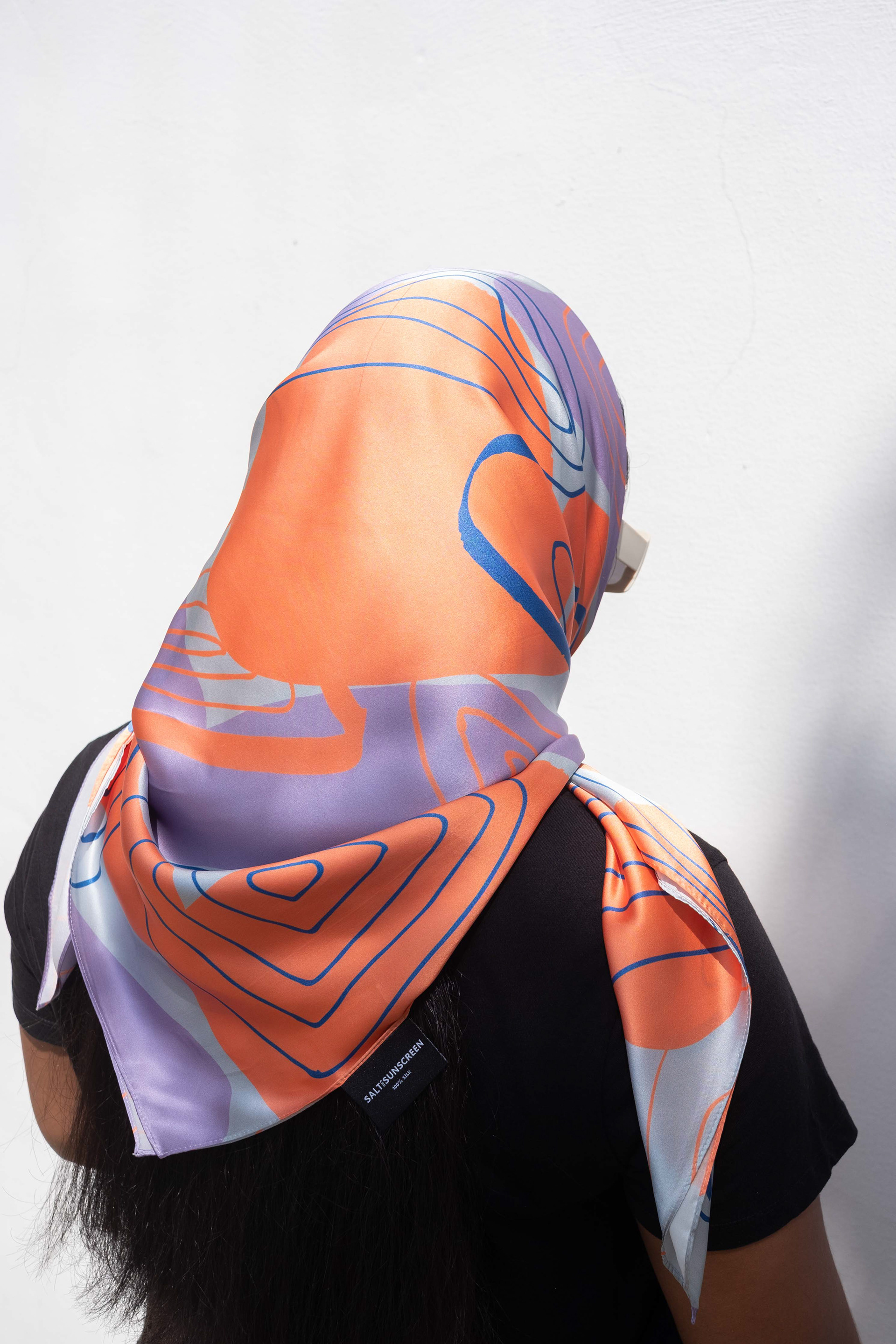 back of a woman covering her head with the printed silk scarf