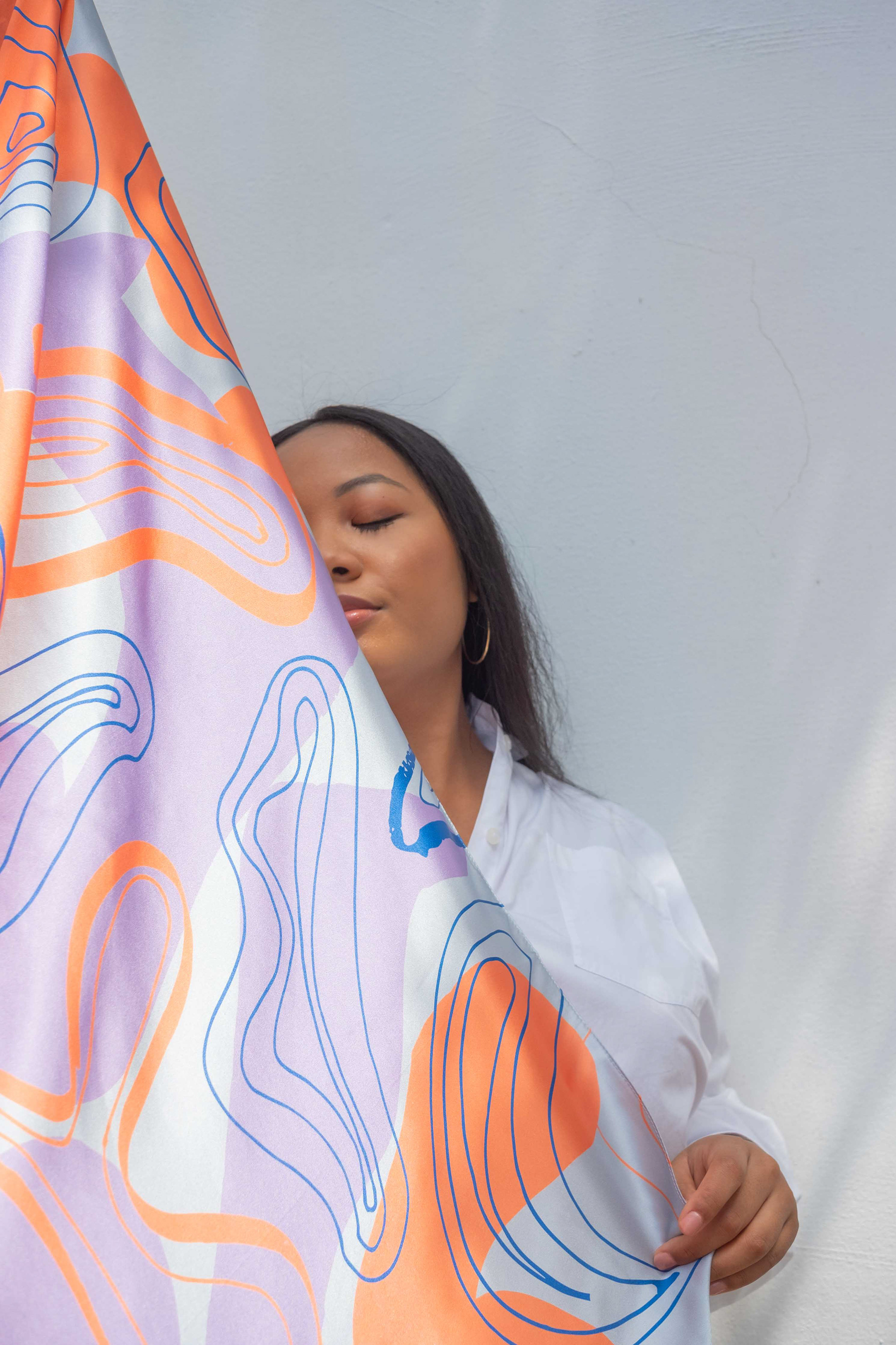 woman covering half of her face with a printed silk scarf