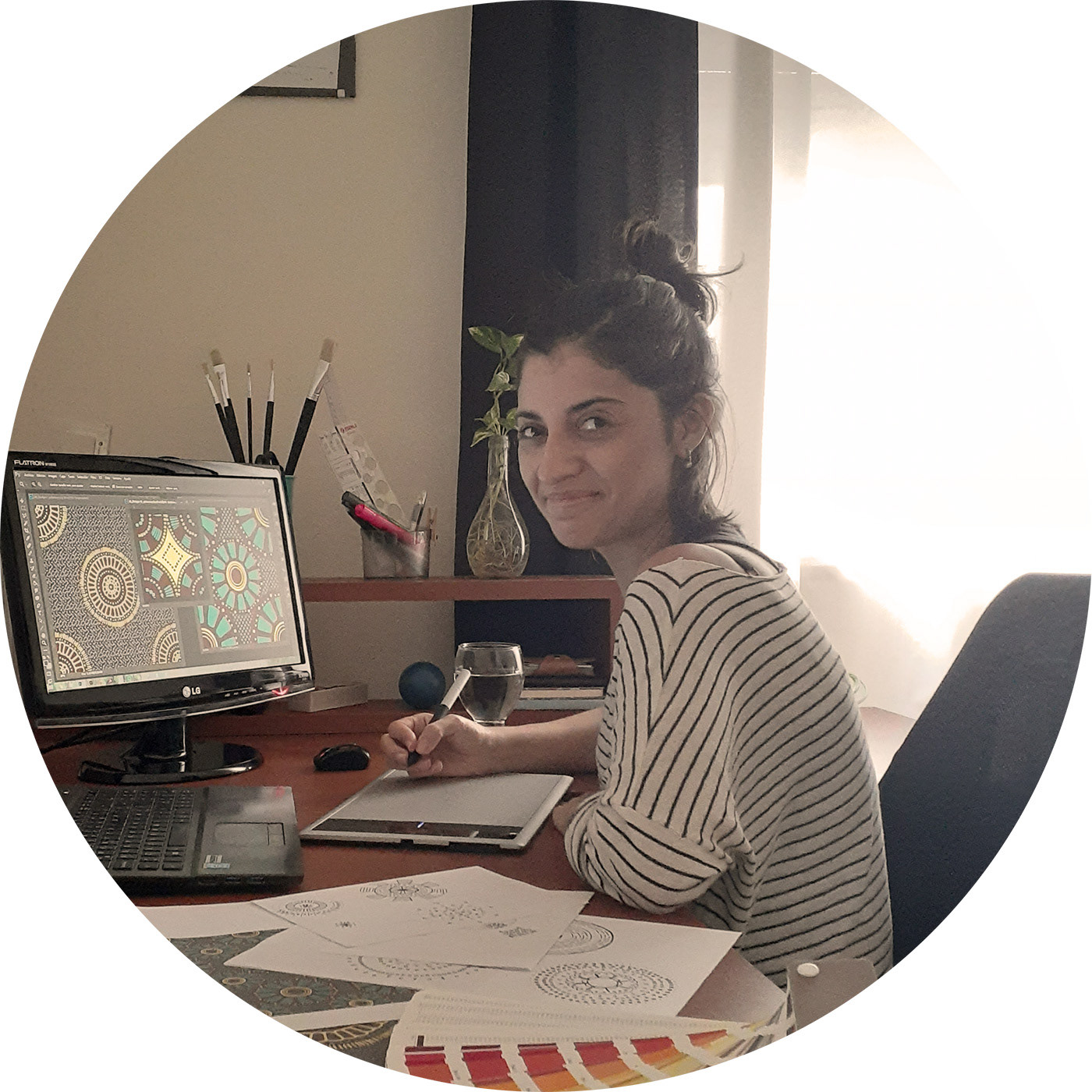 a textile designer woman sitting in her desk using a digitizer tablet with some sketches on the side