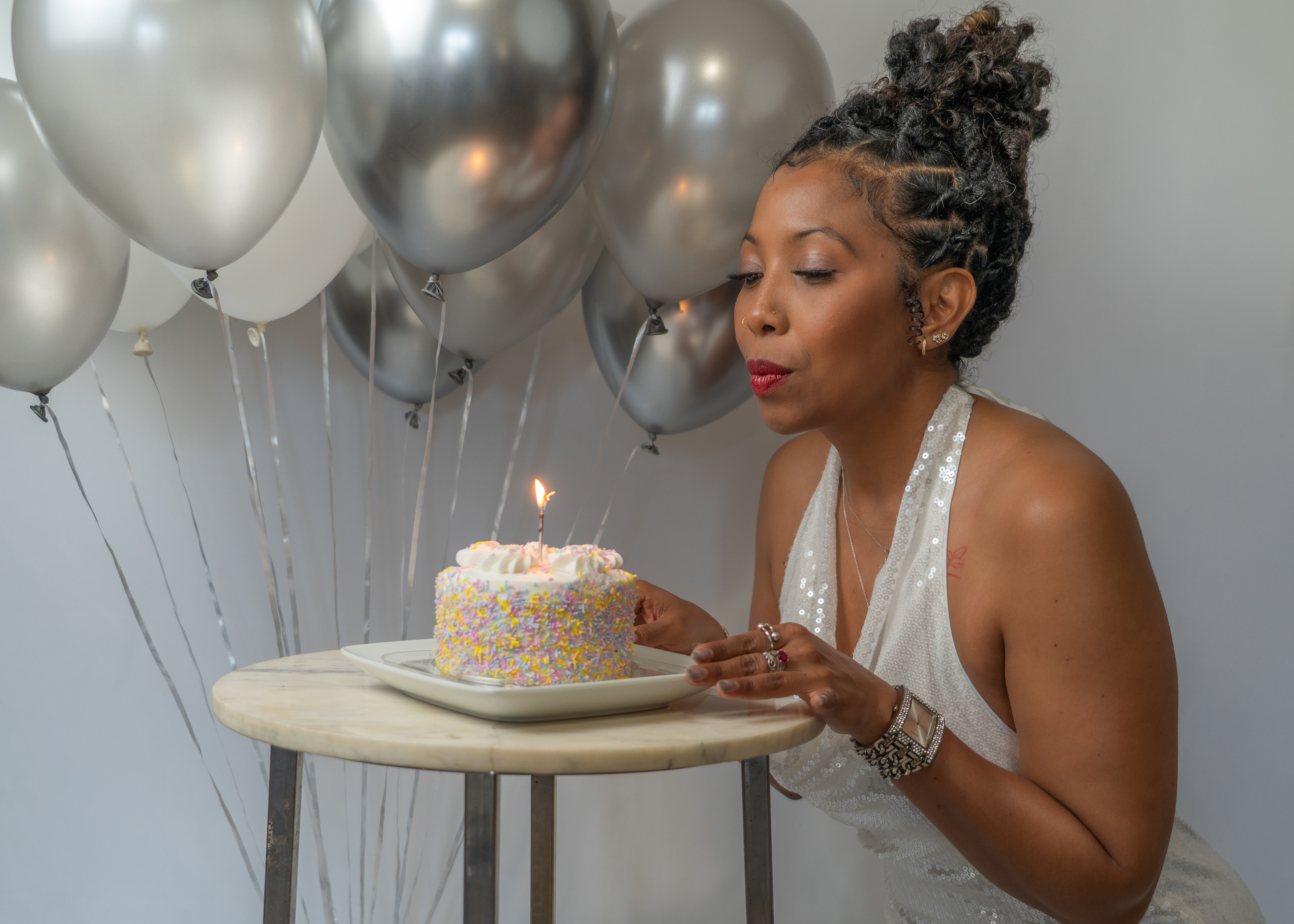 Woman blowing birthday cake in studio shoot, balloon in the background.