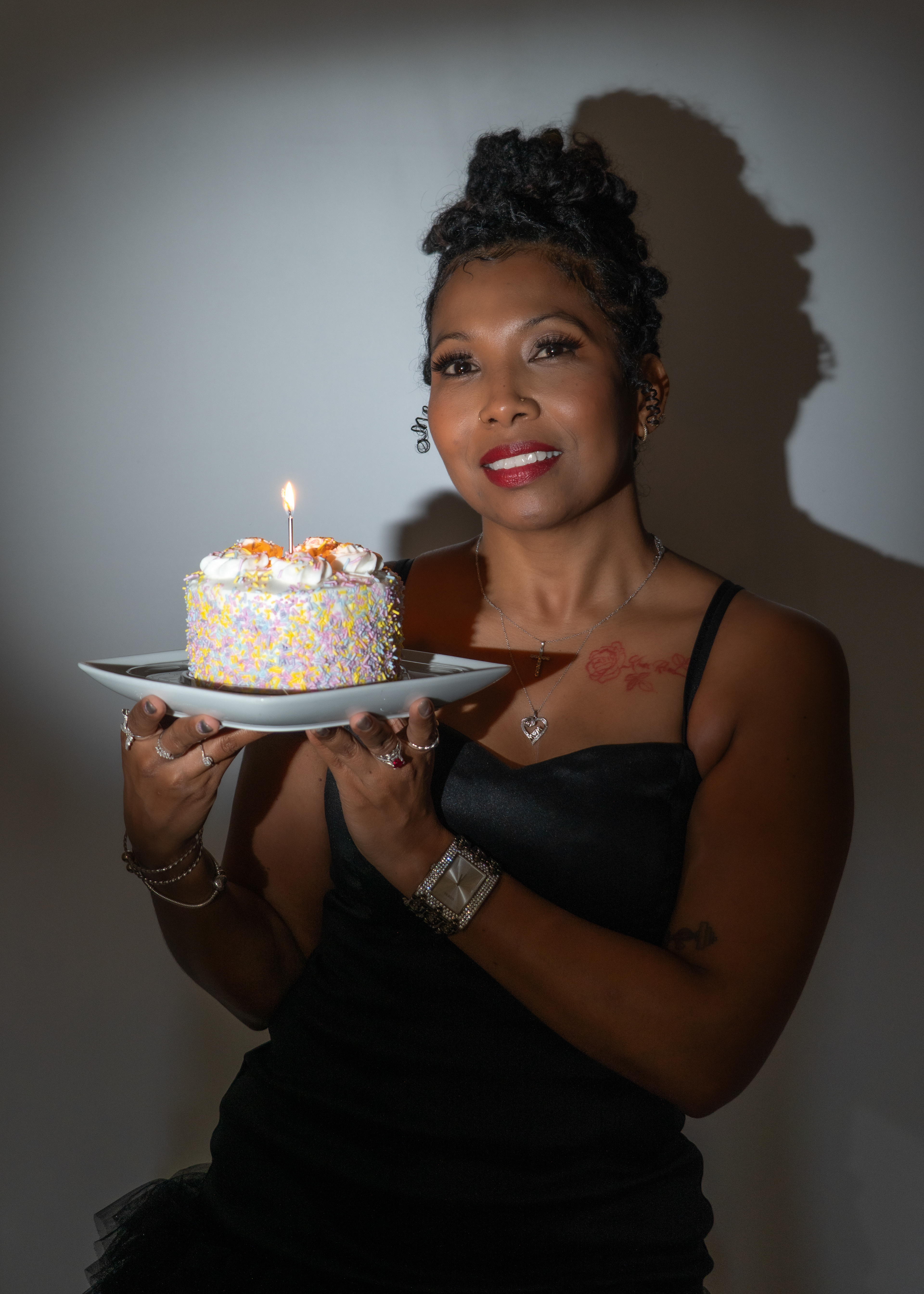 Woman holding cake, posing for birthday shoot in studio.