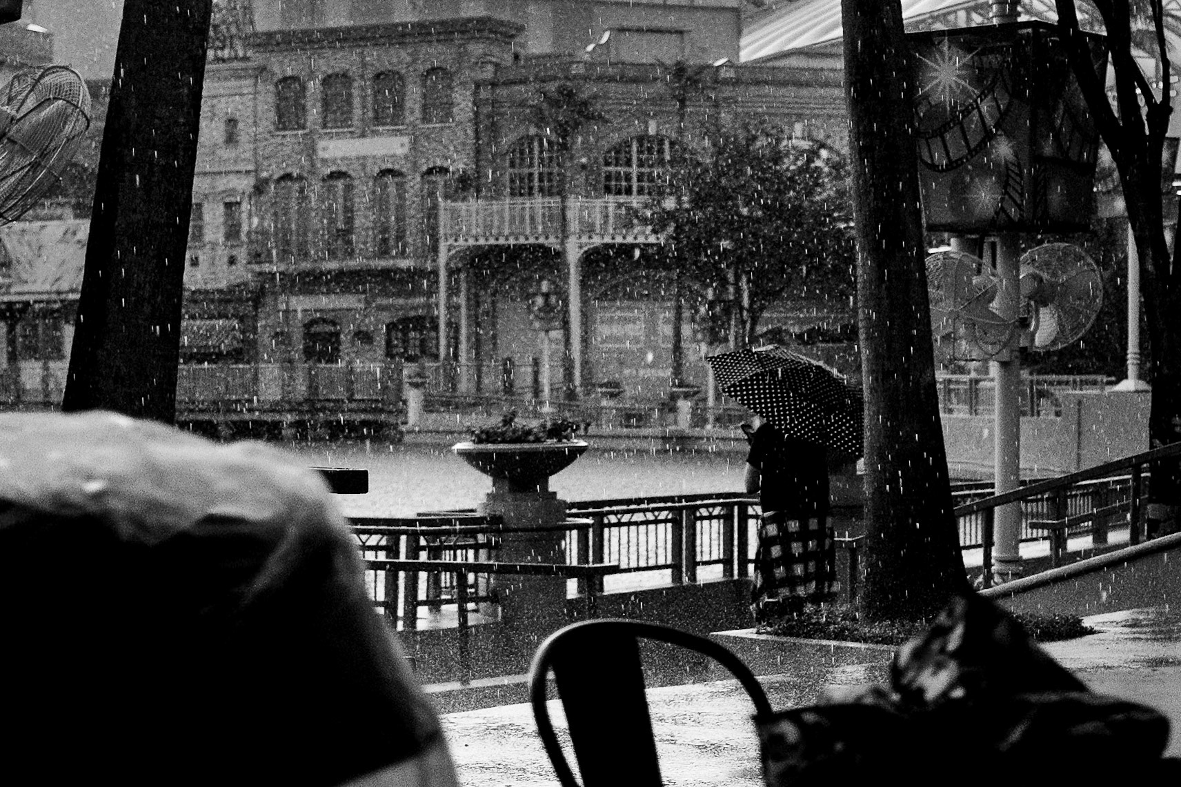 A woman shelters beneath a polka dot umbrella in a downpour, the city emptied by rain. 