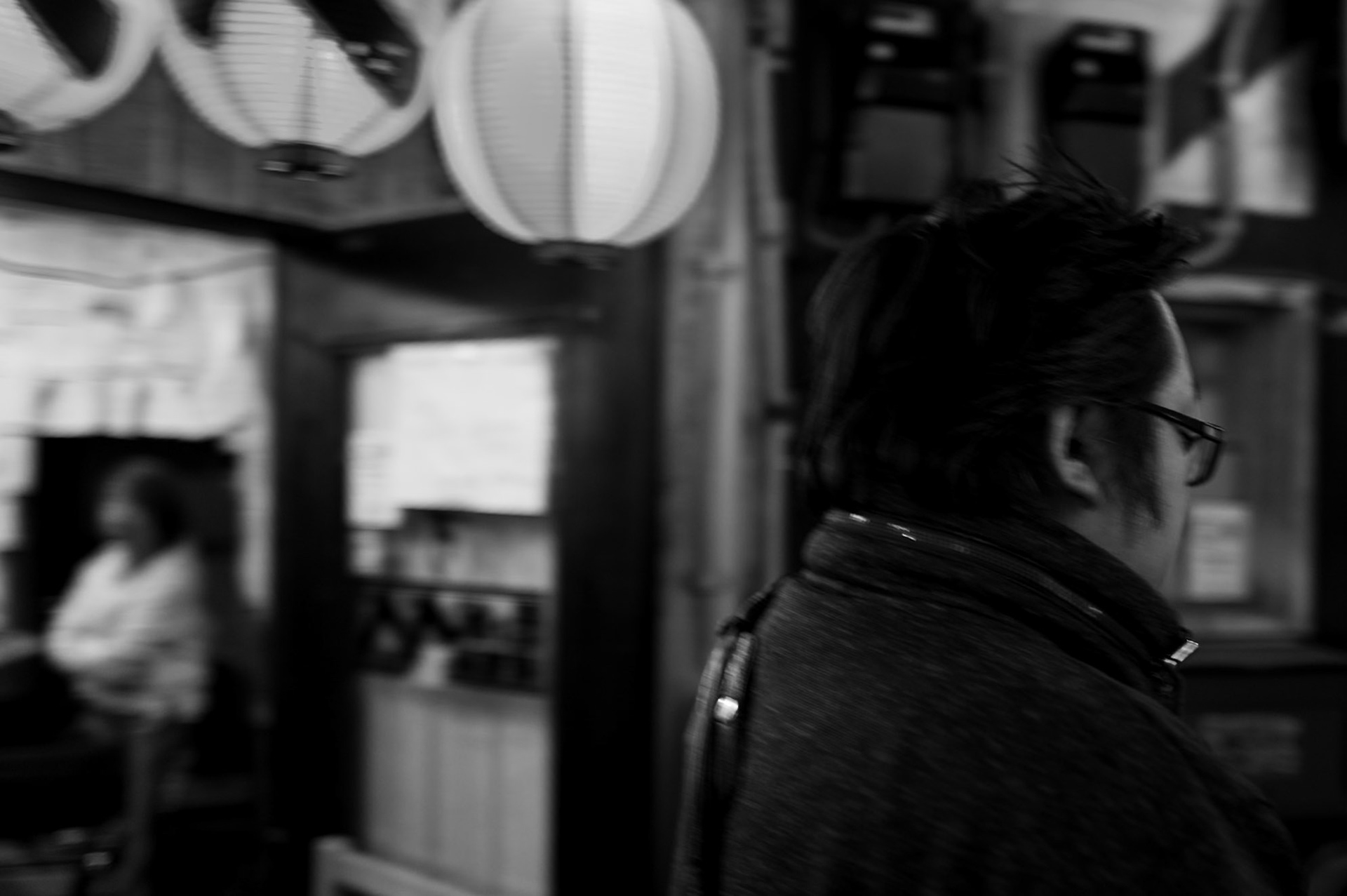 Two people share the same space outside a Tokyo restaurant, each absent from each other. 