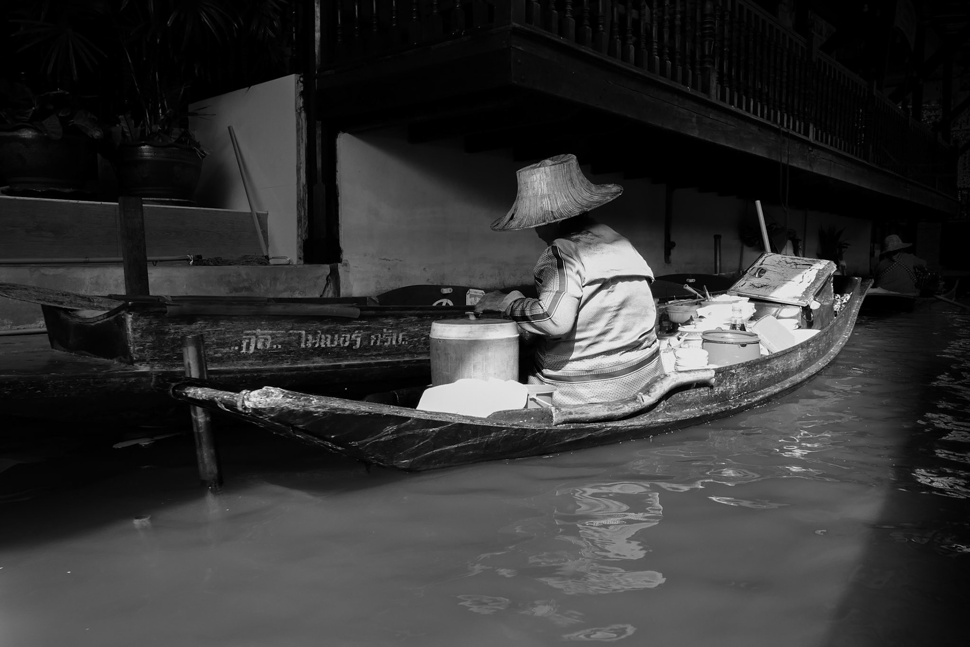 A vendor works alone on her boat, back turned, absorbed in her own world.