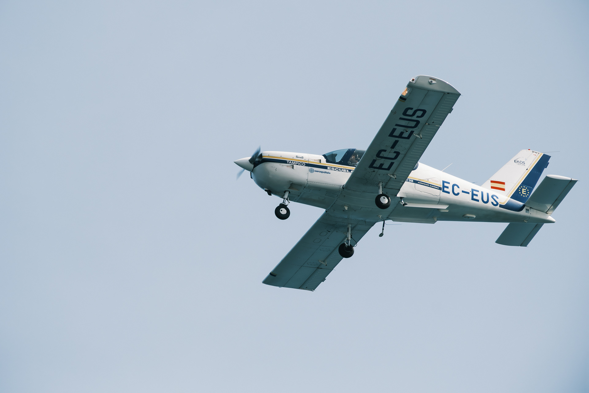 Avioneta blanca y azul con matrícula EC-EUS en vuelo.