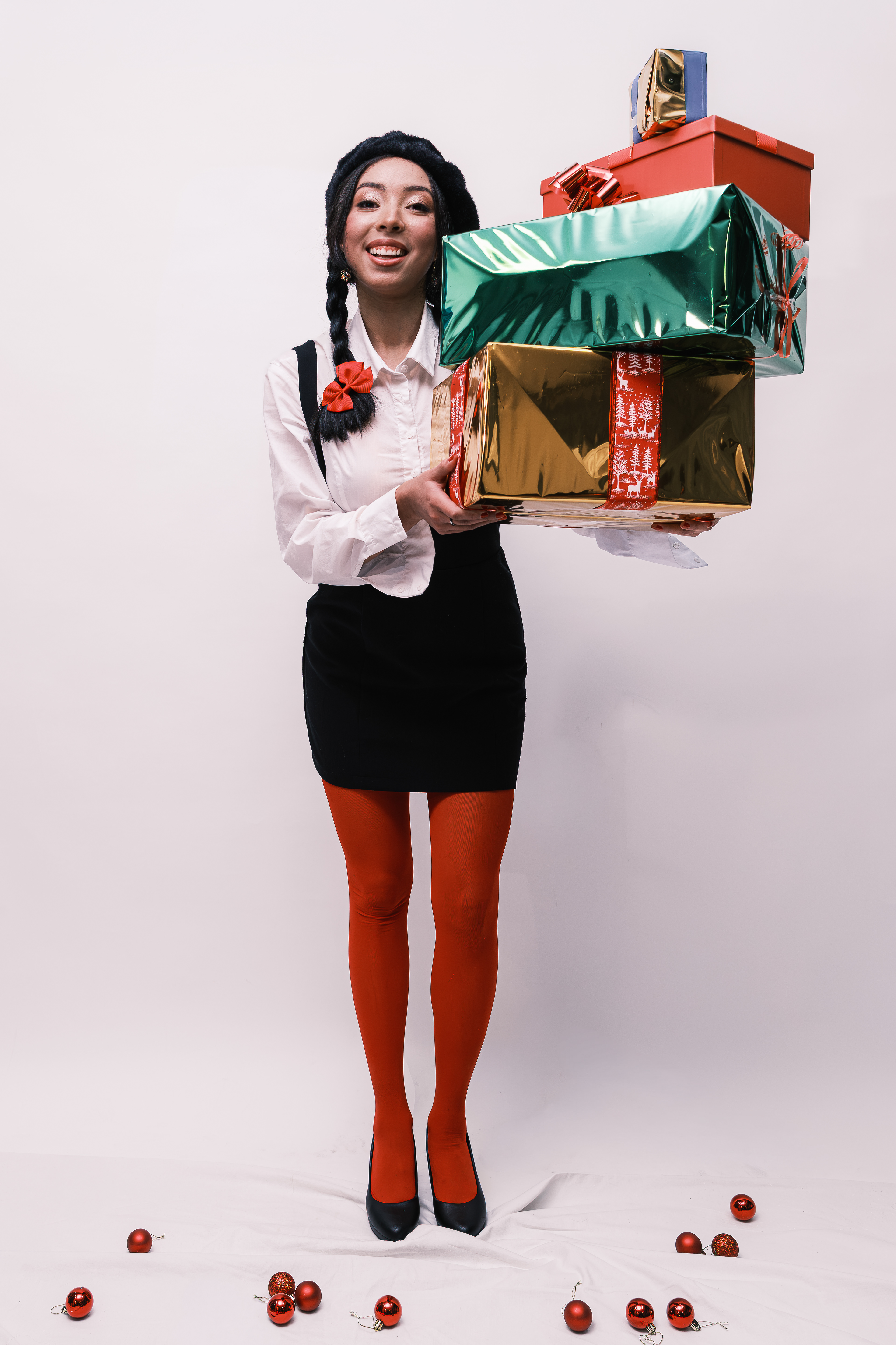 Retrato de cuerpo entero de una mujer con trenzas y medias rojas sosteniendo varios regalos.