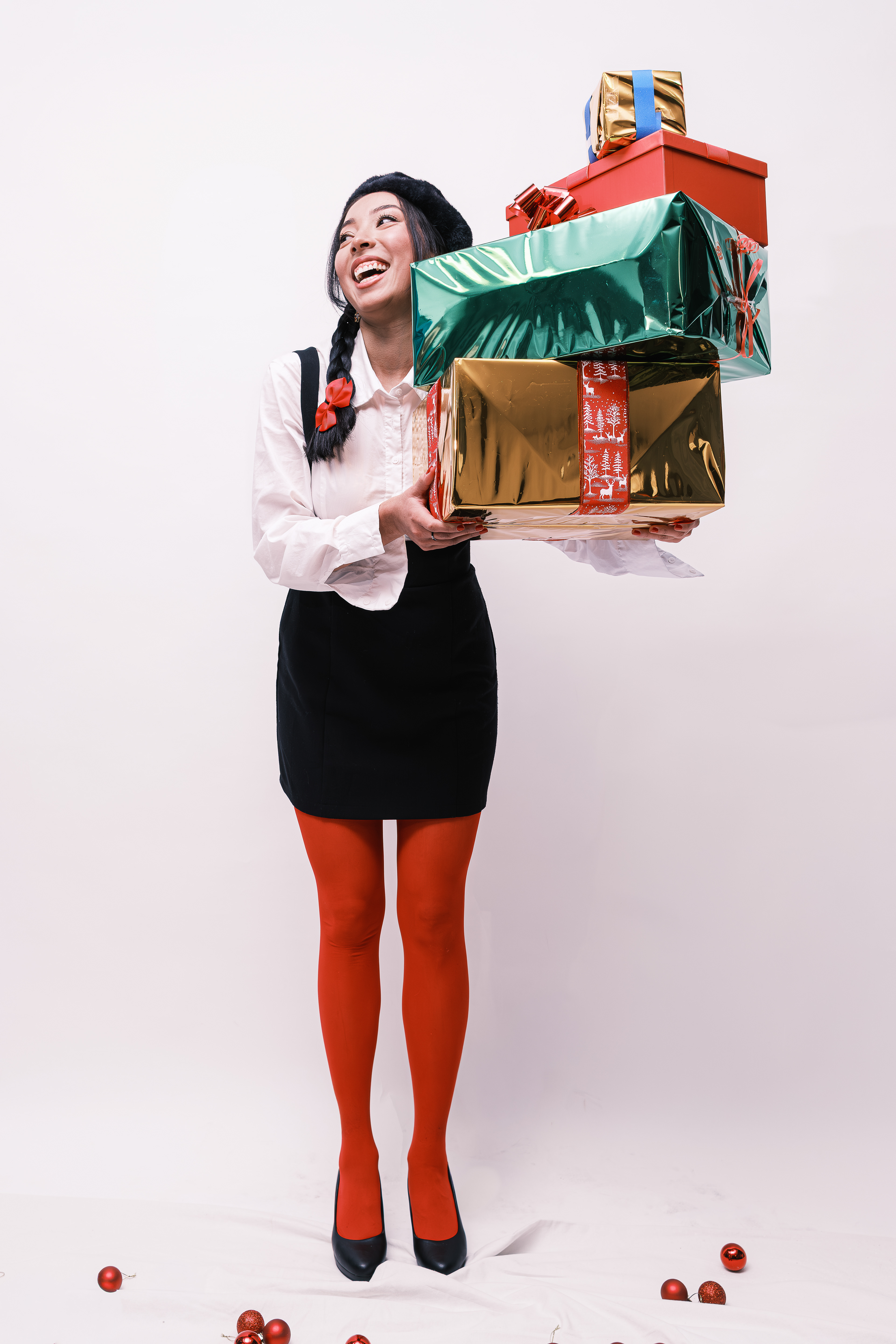 Mujer de pie sosteniendo una pila de regalos envueltos en colores verde, rojo y dorado.