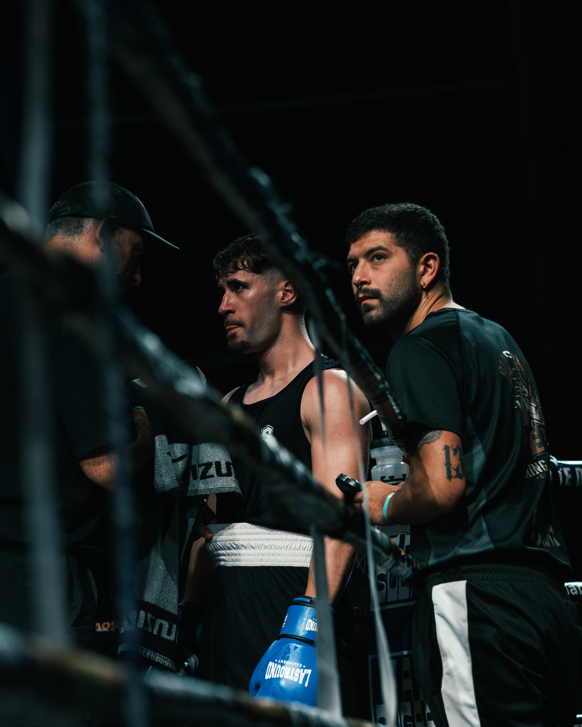 Boxeador de equipación negra junto a su entrenador en una esquina del ring.