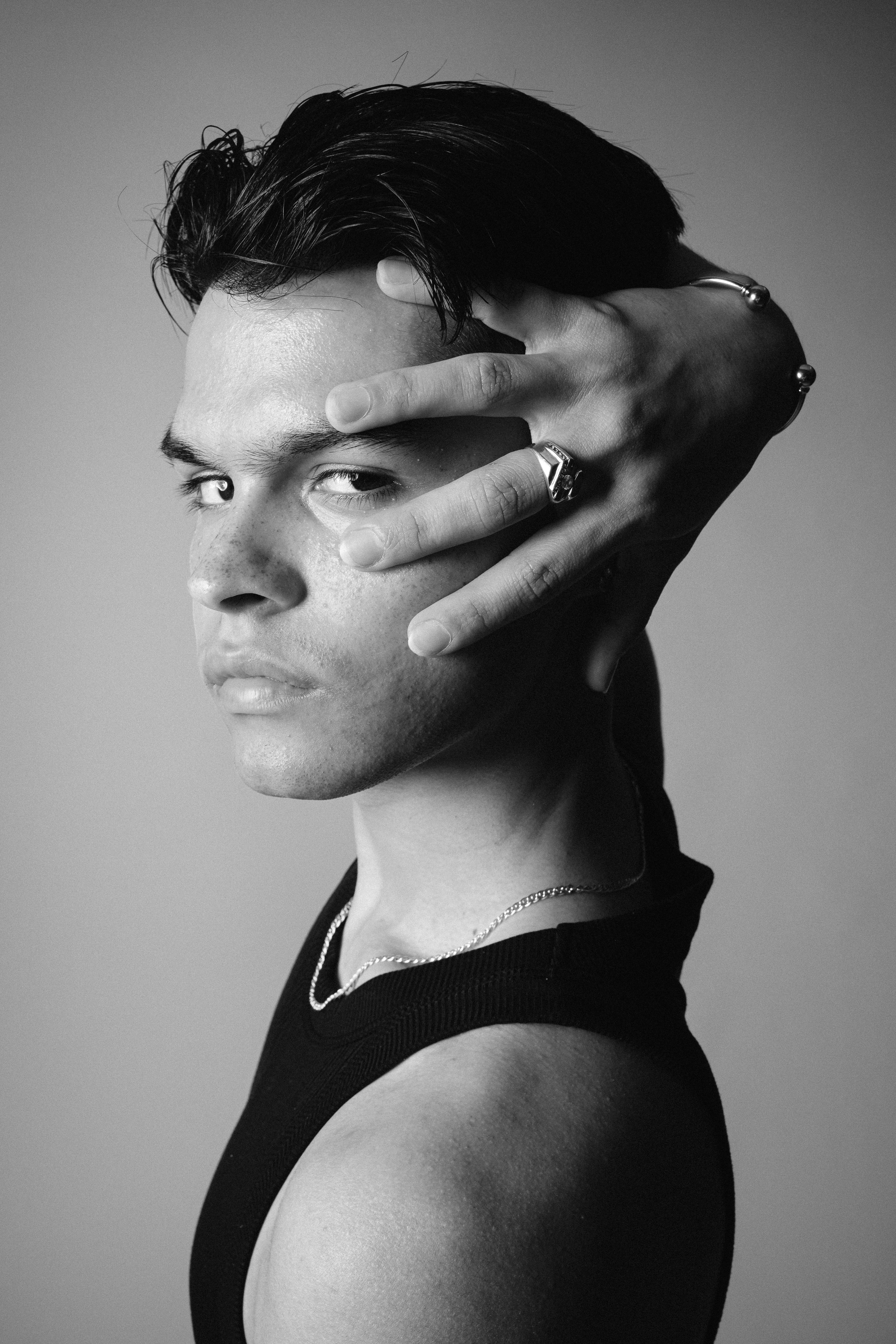 Primer plano en blanco y negro de Bryan mirando a cámara, con una mano junto al rostro y los dedos extendidos sobre la frente.