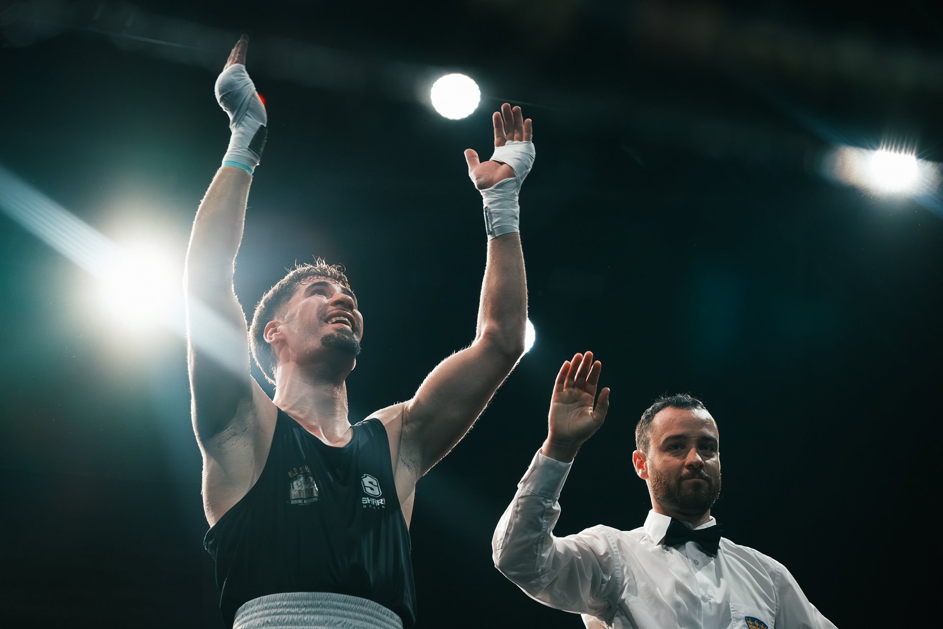 Boxeador levantando ambas manos vendadas junto al árbitro al terminar el combate.