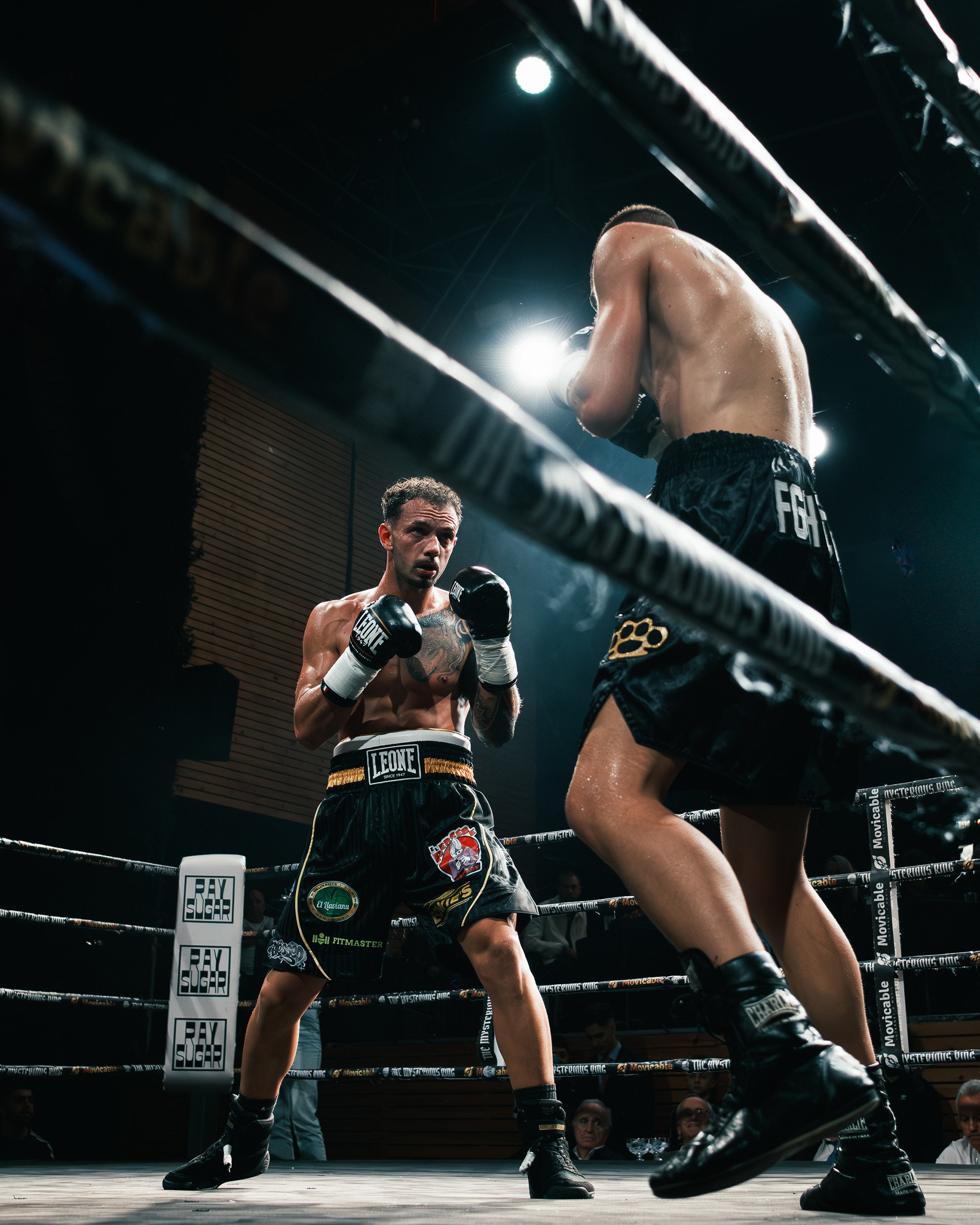 Boxeador profesional en guardia frente a un rival de espaldas dentro del ring.
