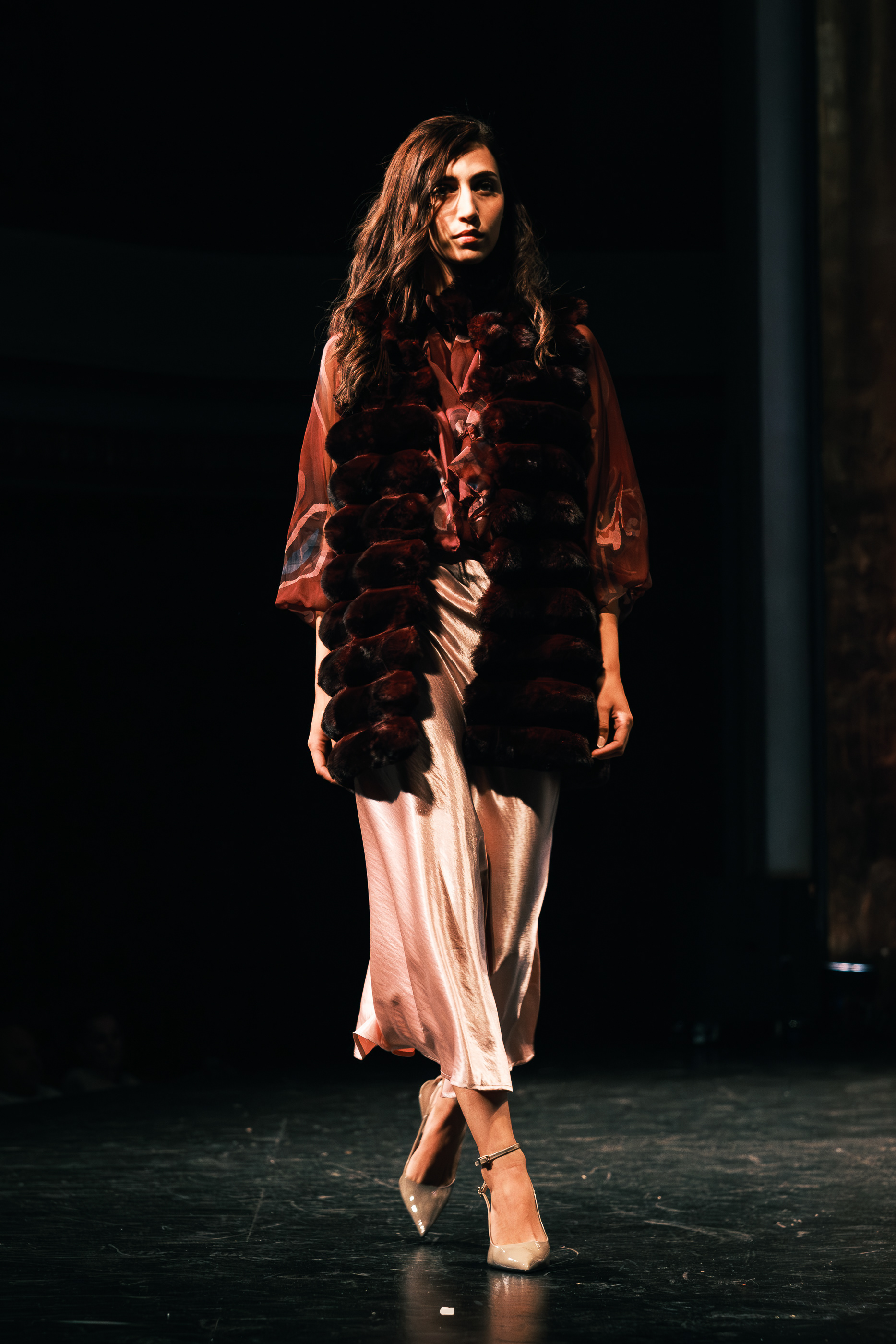 Modelo desfilando con abrigo oscuro de textura voluminosa y falda clara en Asturias Fashion Week.