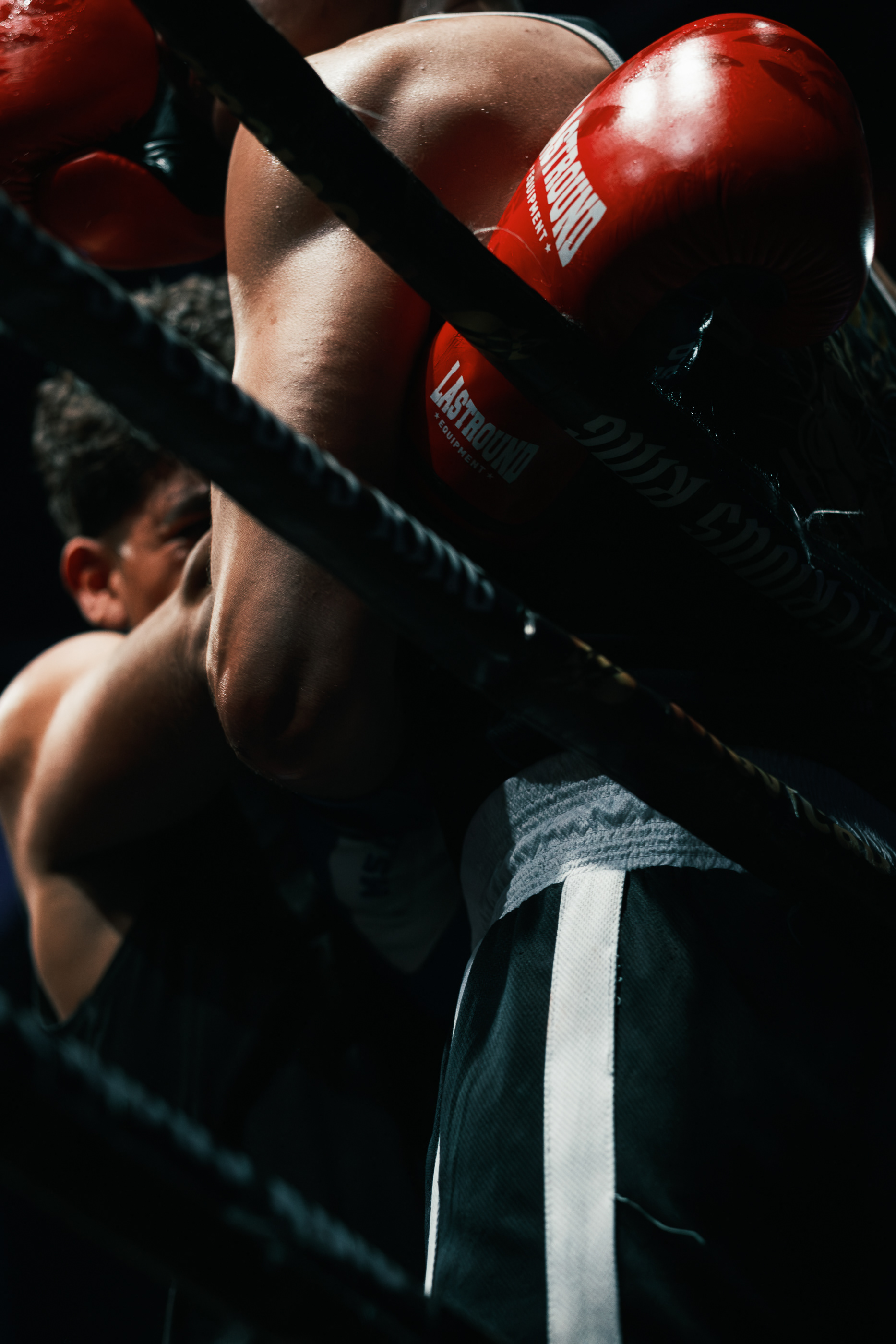Boxeador con guantes rojos apoyado en las cuerdas mientras recibe indicaciones en su esquina.
