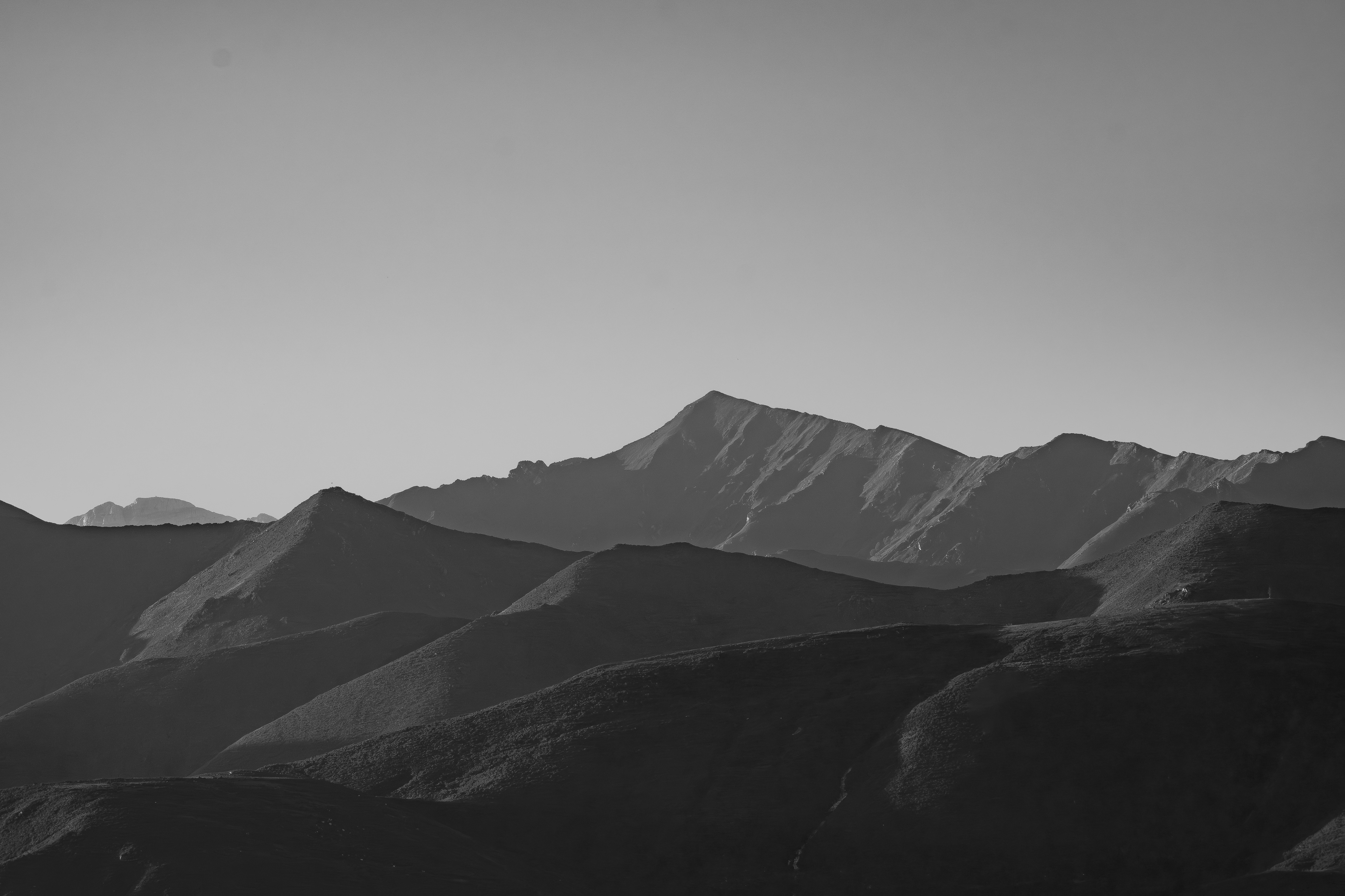 Sucesión de laderas y un pico pronunciado con luz lateral, en blanco y negro.