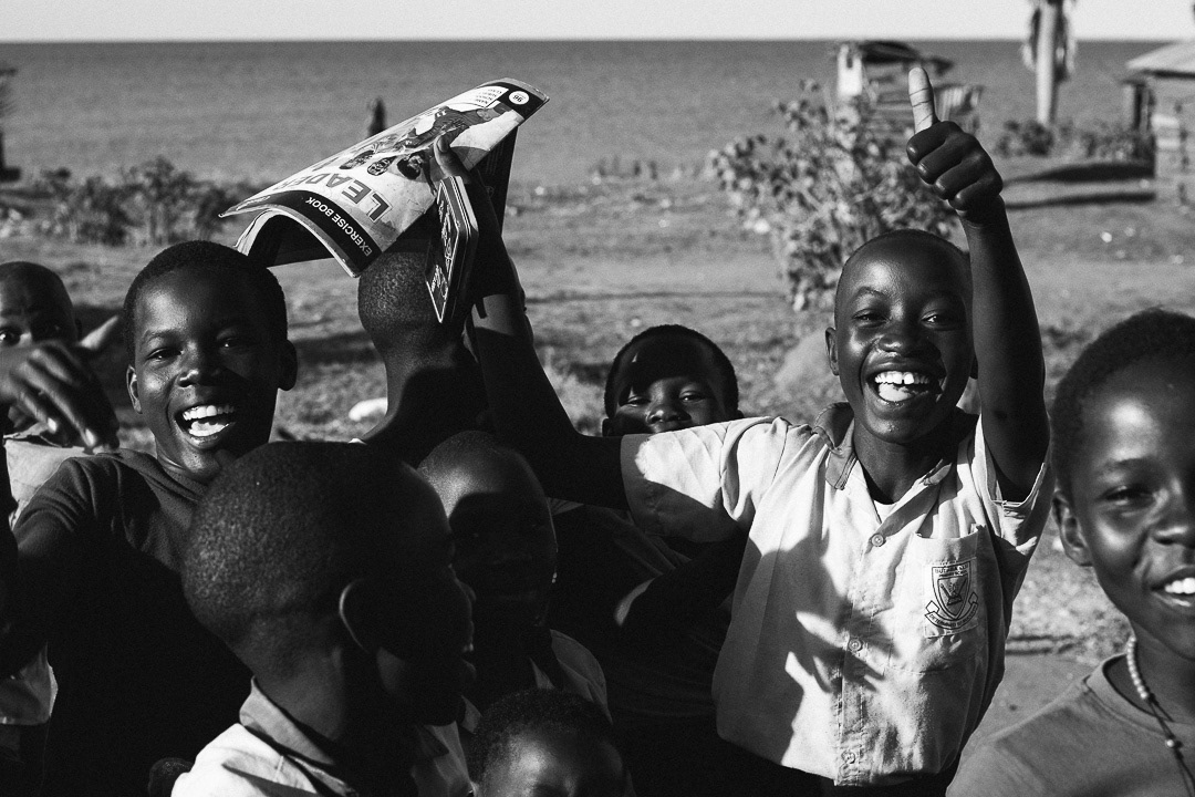 Grupo de niños sonrientes levantando los brazos en Uganda, en blanco y negro.