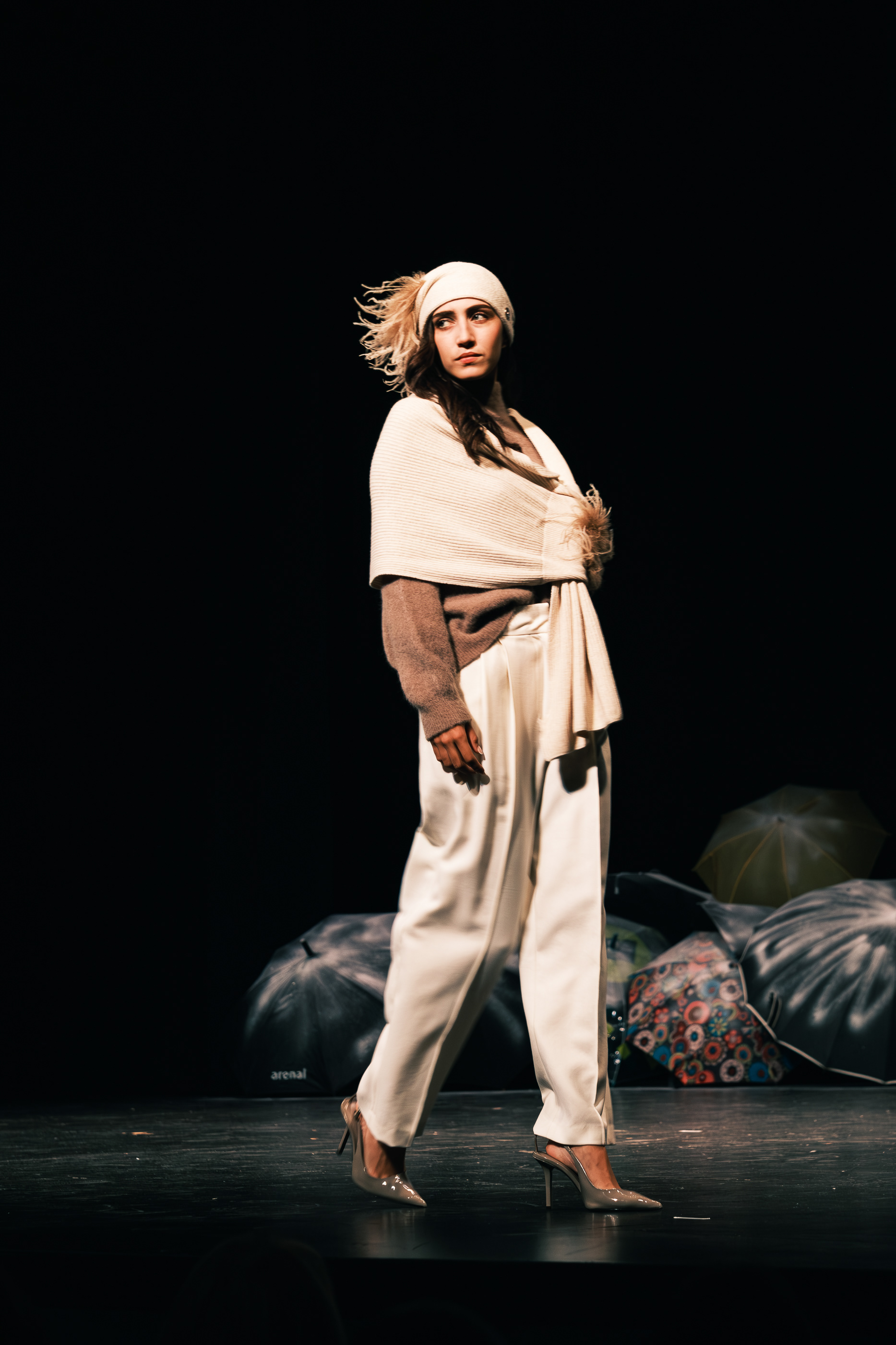 Modelo desfilando con gorro claro, capa beige y pantalones blancos.