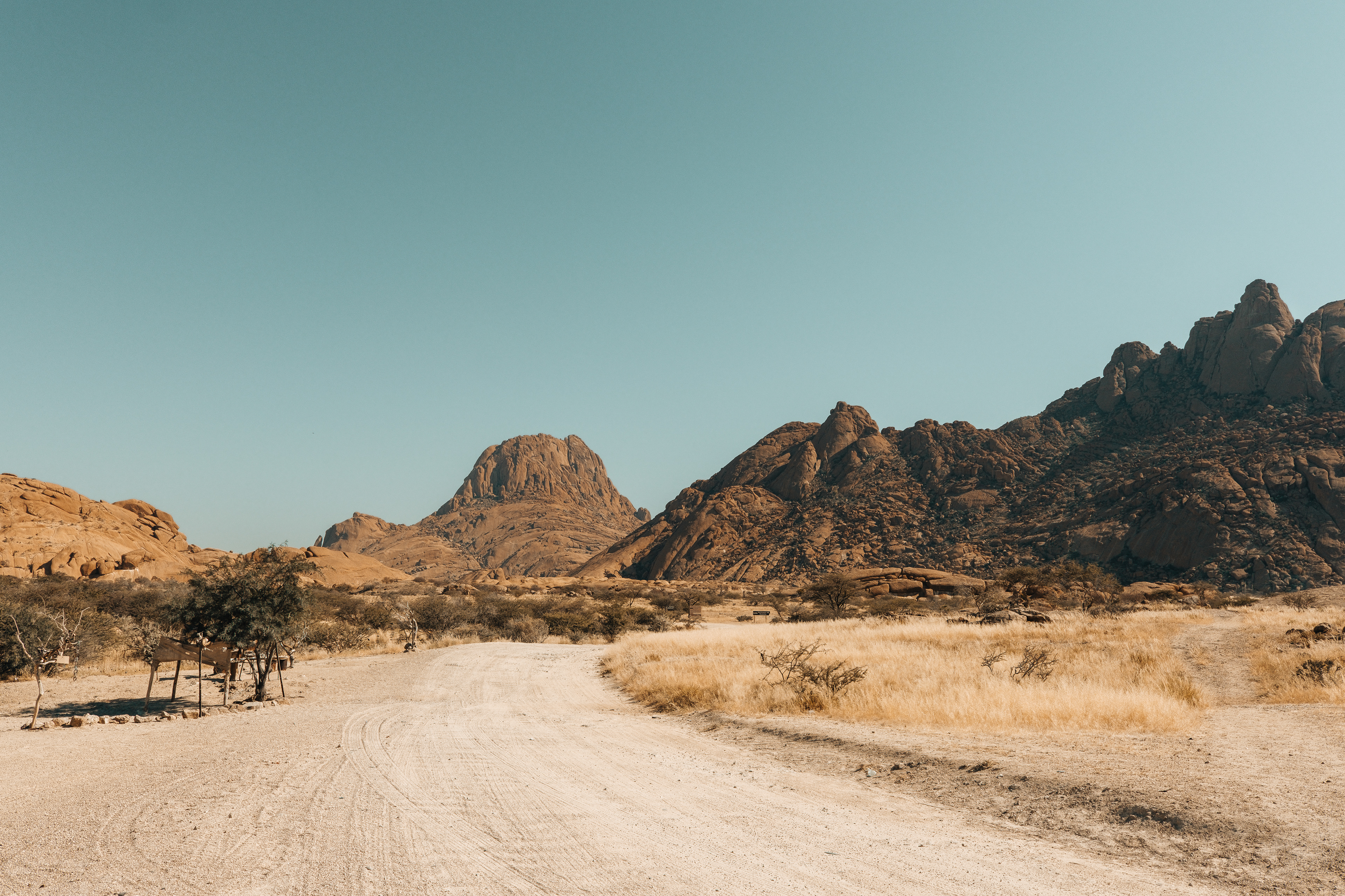 Camino de tierra entre montañas de granito y hierba seca.